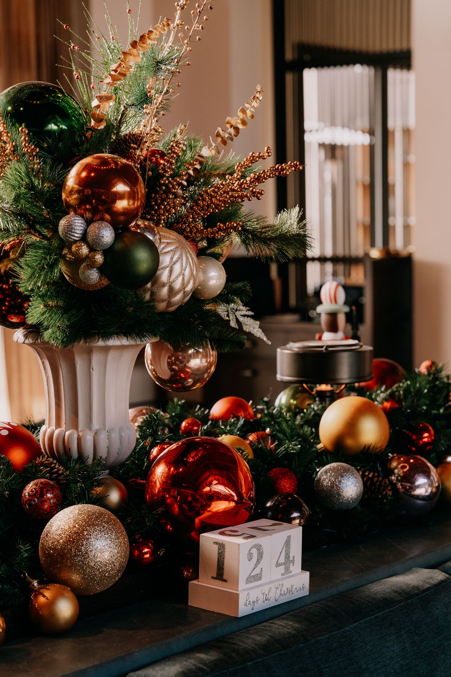 Elegant Christmas decorations featuring copper, gold and silver ornaments with greenery arranged on a dark surface.