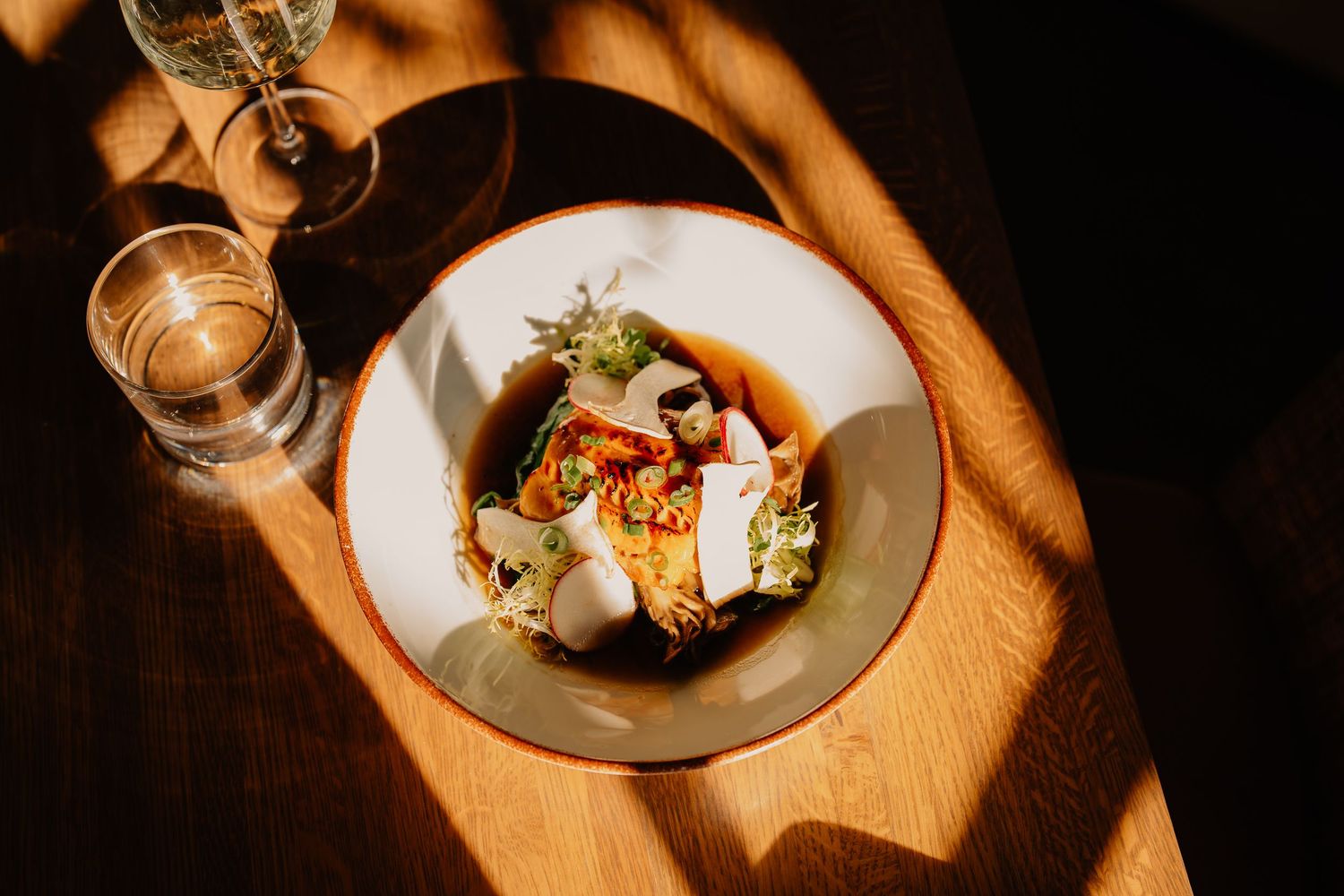 Sunlight casts dramatic shadows on plated gourmet dishes in an elegant restaurant setting.