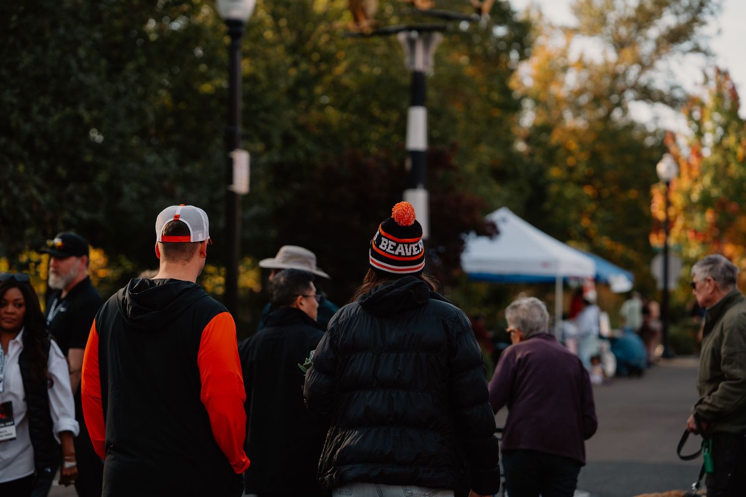 A crowd of people gather at an outdoor event during dusk with tents in the background.