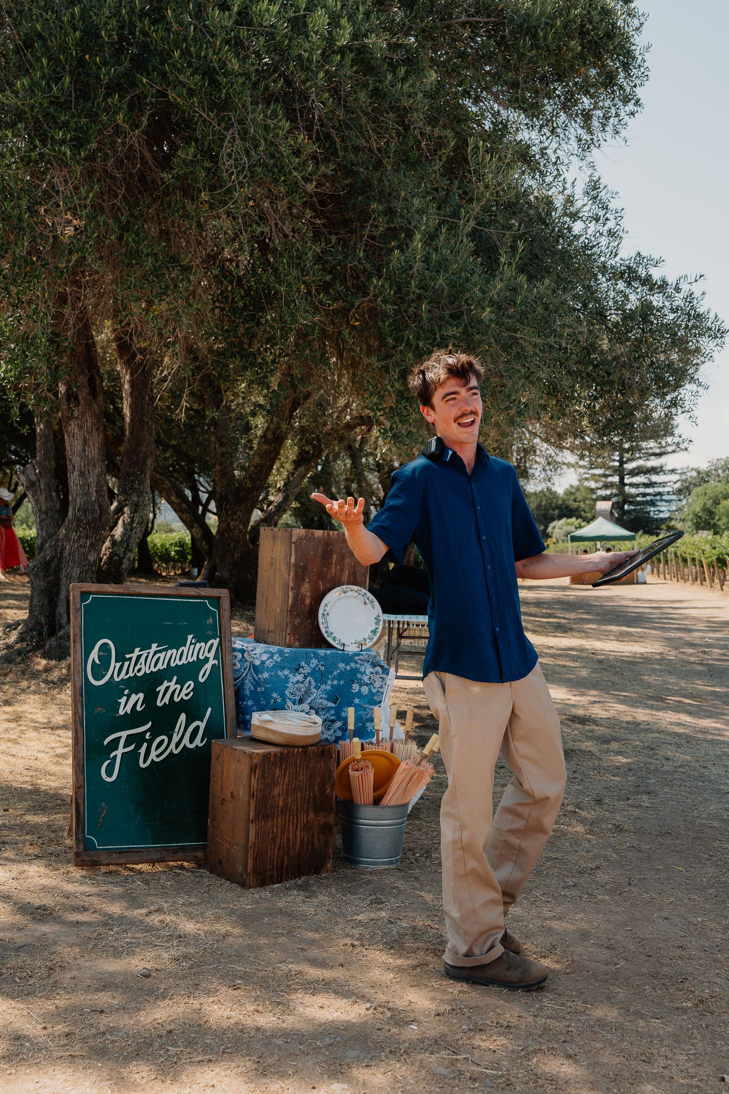 Sequence of candid outdoor photos under olive trees with vintage decor and teal signage for special event setup.