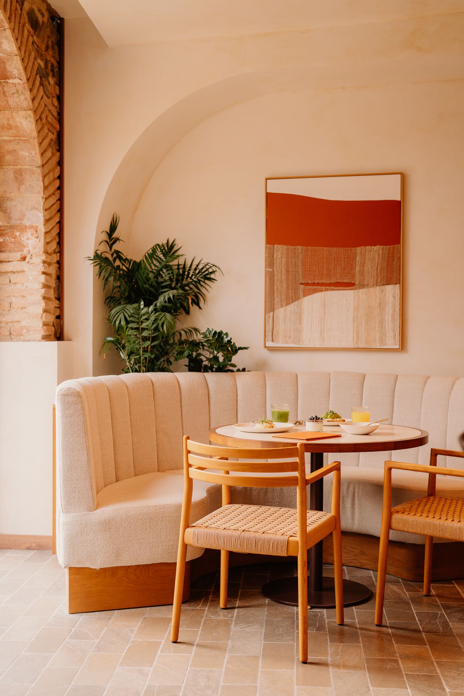 Modern restaurant interior with curved banquette seating, wooden chairs, round table and abstract orange wall art.