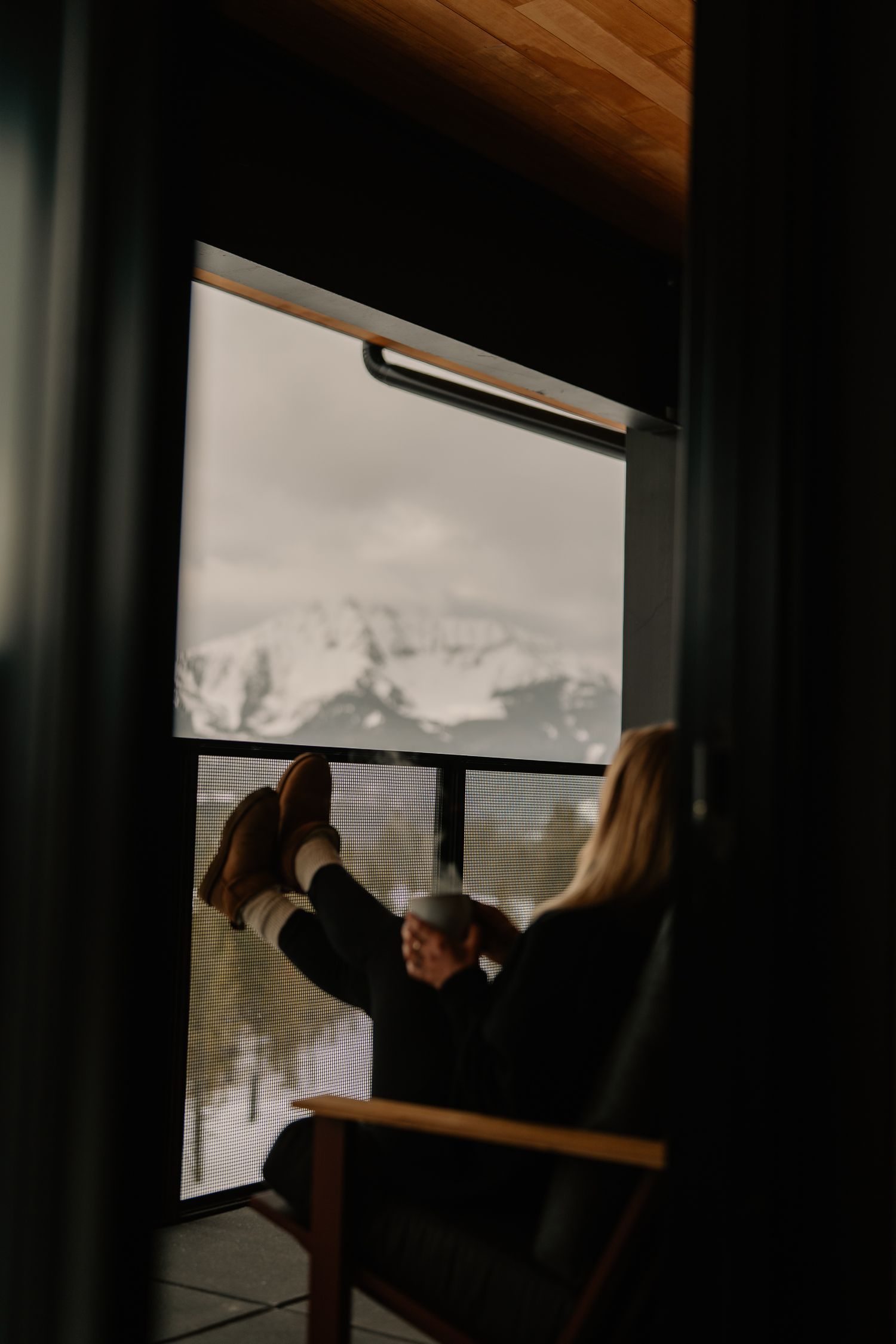 Dark silhouettes frame a window view of snowy mountain landscapes in a cozy cabin setting.