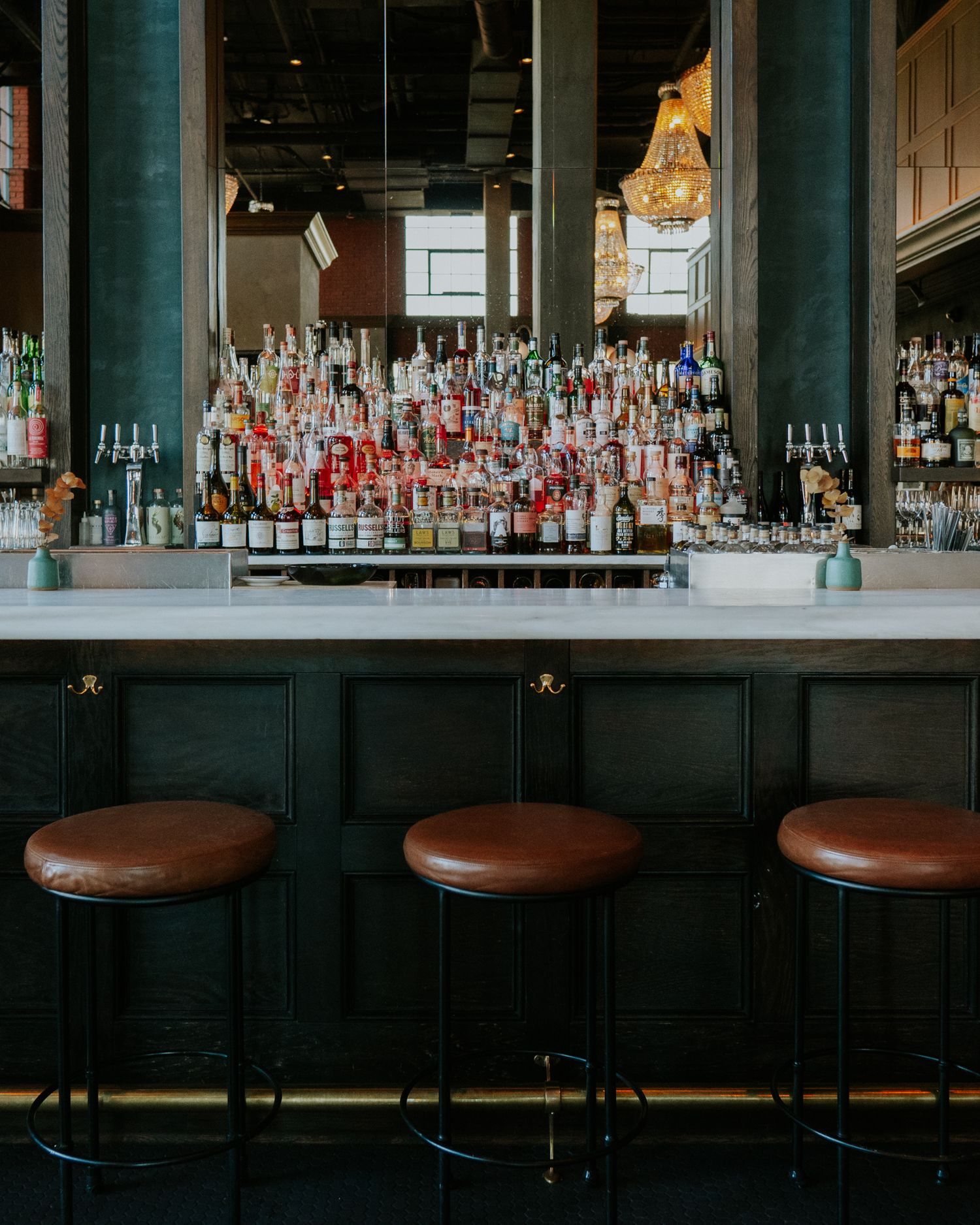 Dark wood bar with leather stools showcasing an extensive collection of liquor bottles on illuminated shelving.