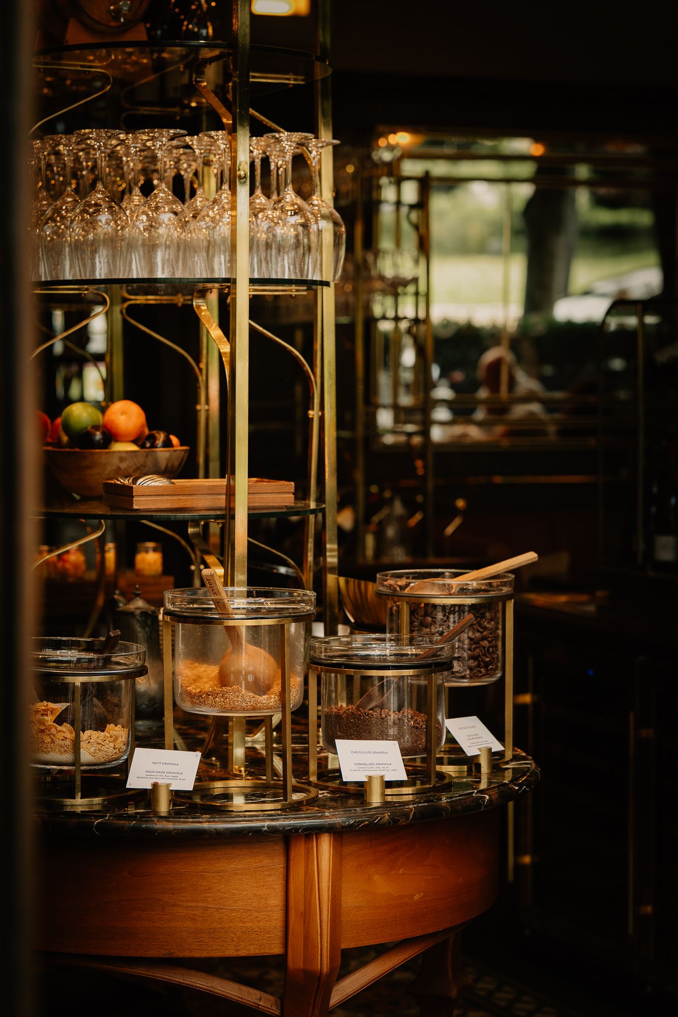 Elegant gold buffet display with glass jars, wine glasses, and fresh fruit on a marble table in a luxury restaurant.