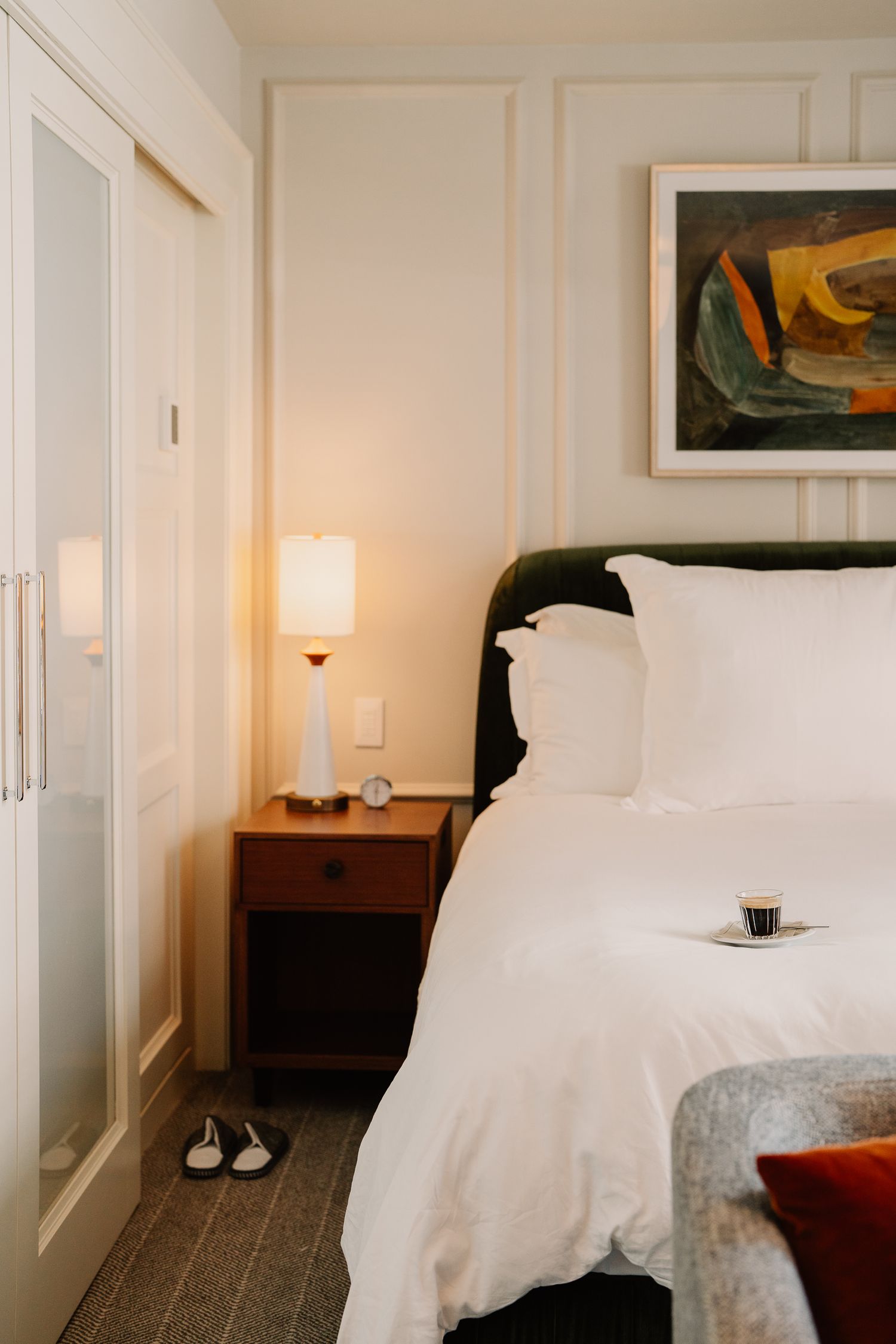 Luxurious hotel bedroom with crisp white bedding, wooden furniture, and wall art in soft lighting.