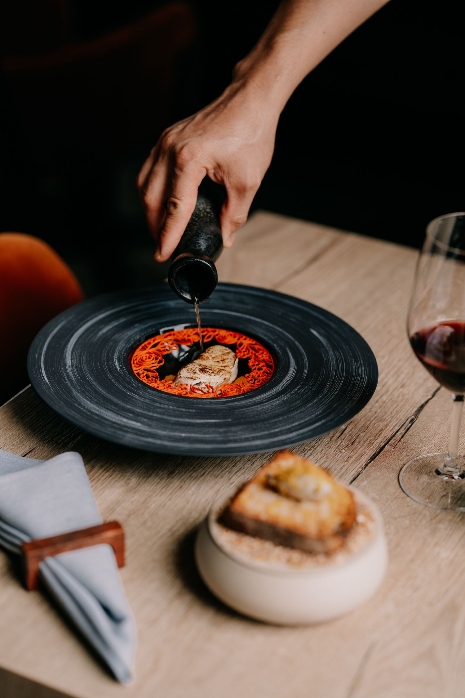 Hands plating food on black circular plates against a dark background with dramatic lighting.