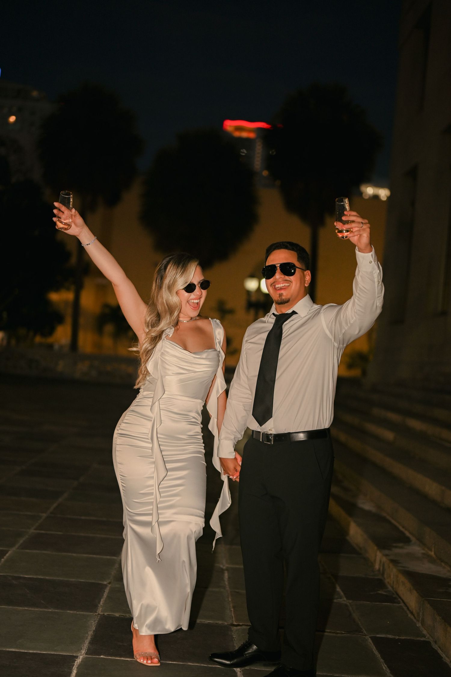 A couple dances playfully on stone steps at night, with the woman in a white dress raising her arms.