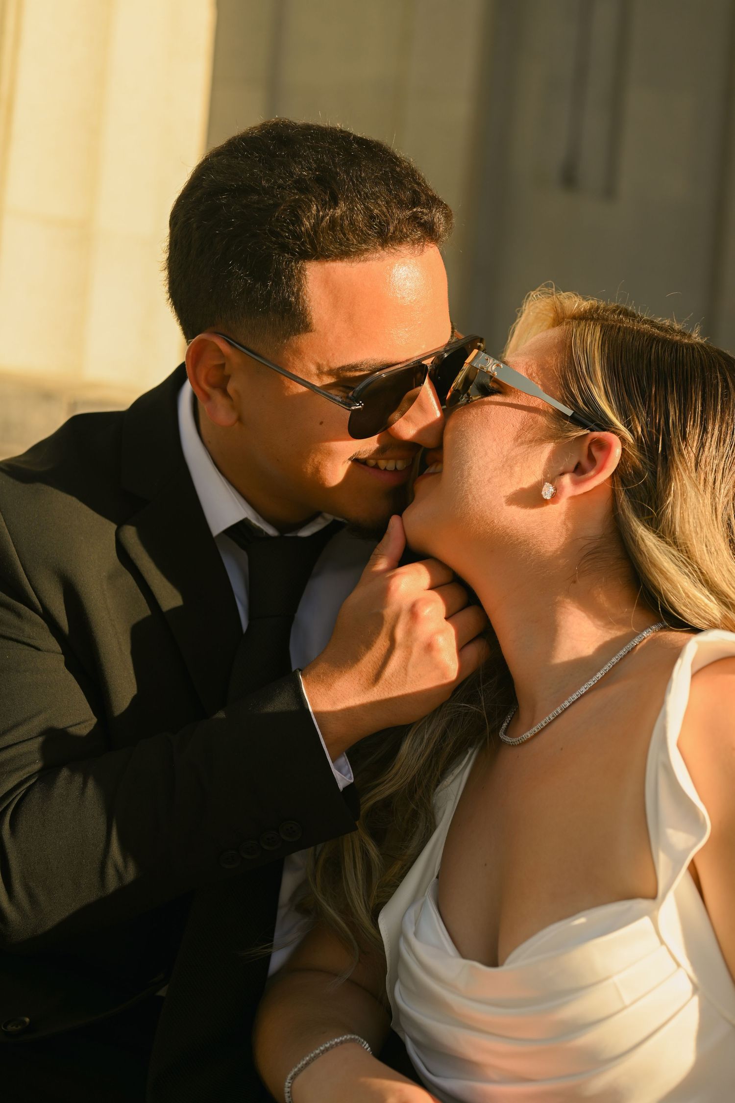 A romantic couple in formal attire share a tender kiss in warm evening lighting.