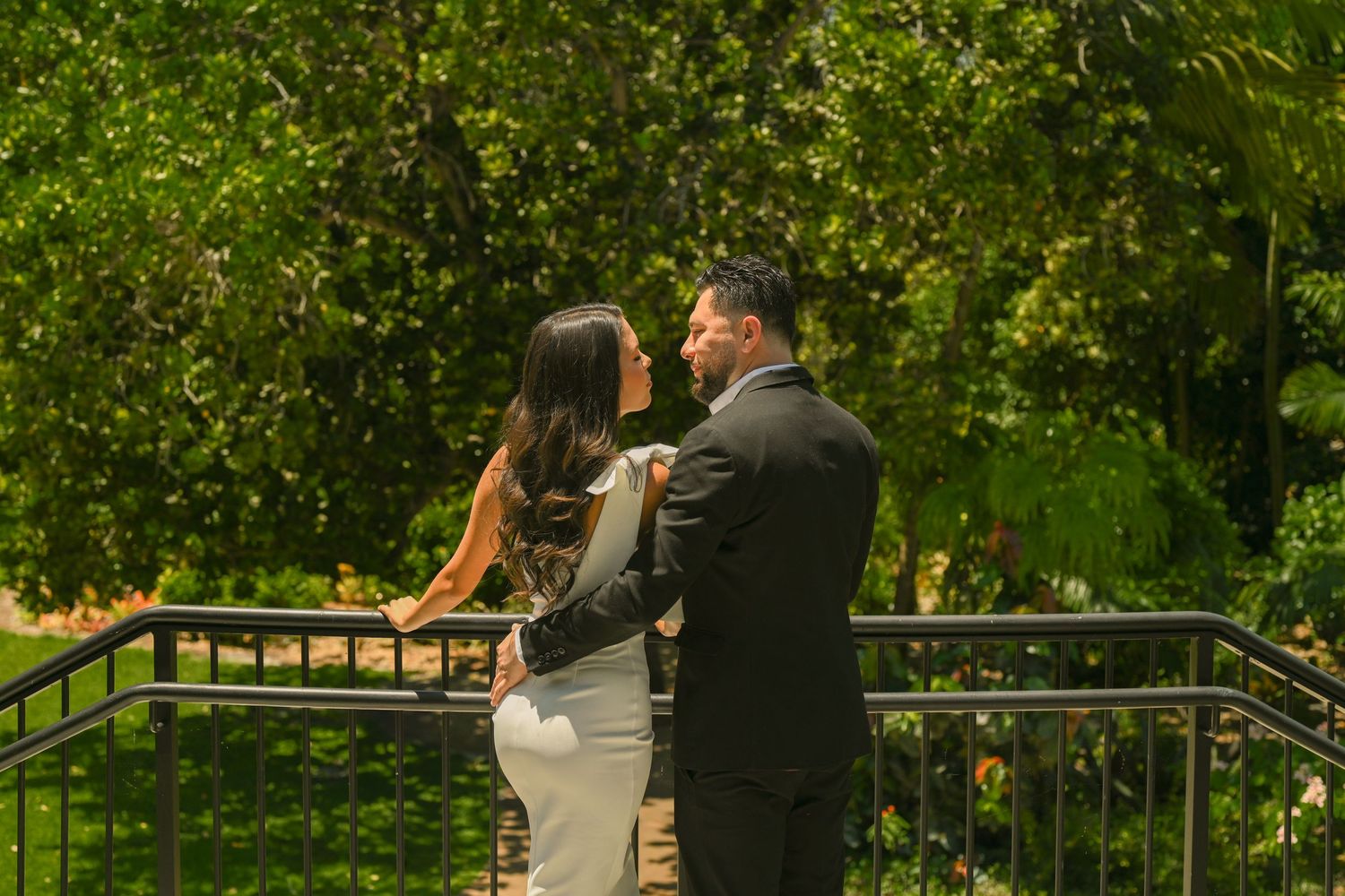 A couple interacts playfully on an outdoor balcony with green foliage.
