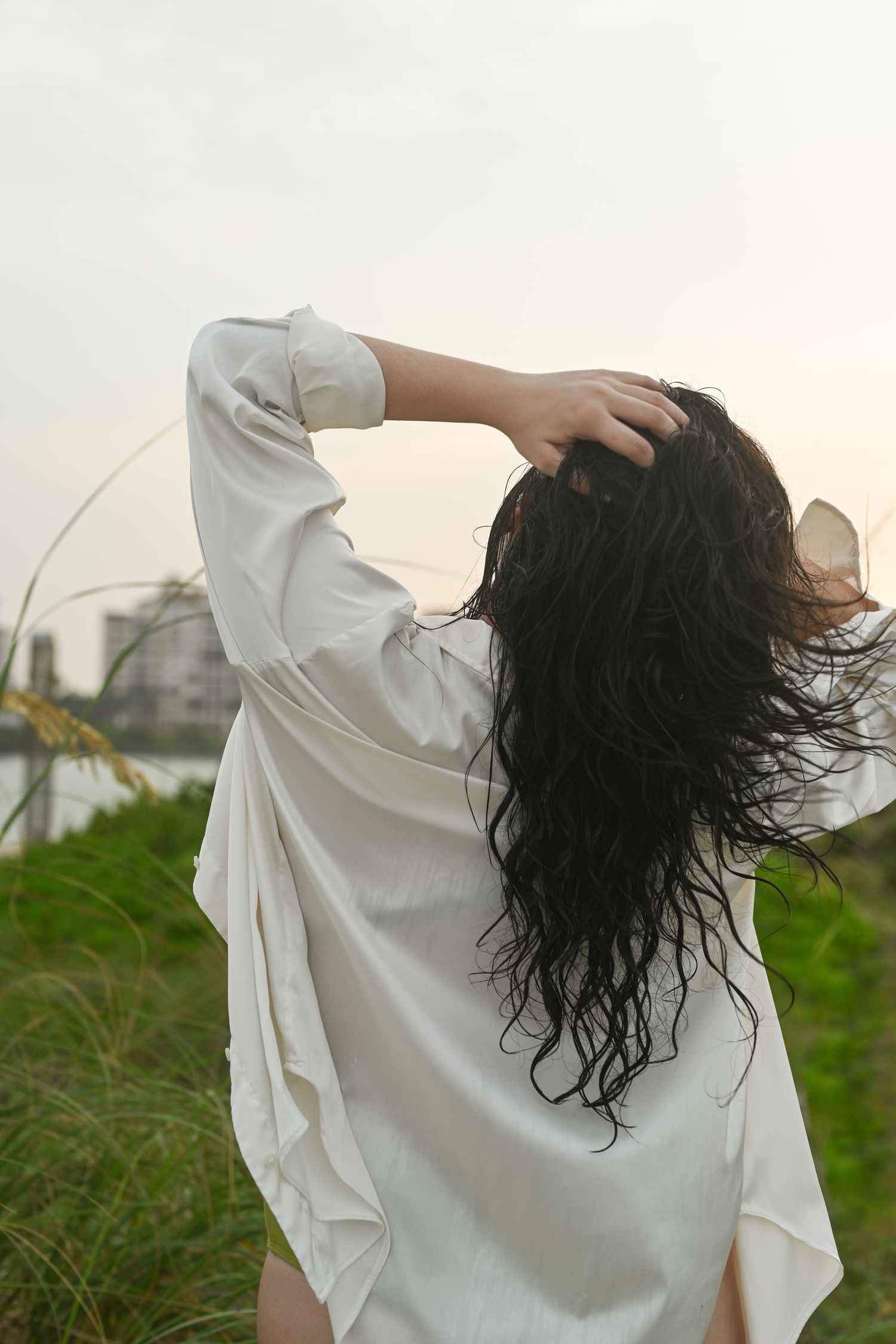 Person in white shirt tosses wet hair against cloudy sky.