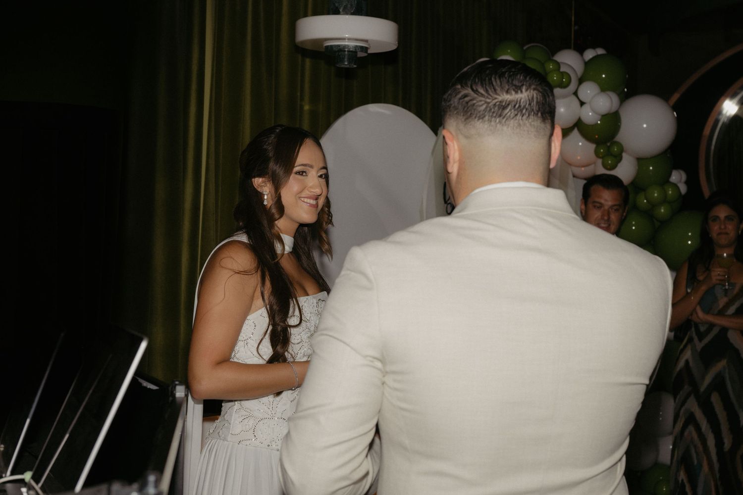 Couple exchanging vows at a wedding ceremony with green and white balloon decorations in the background.