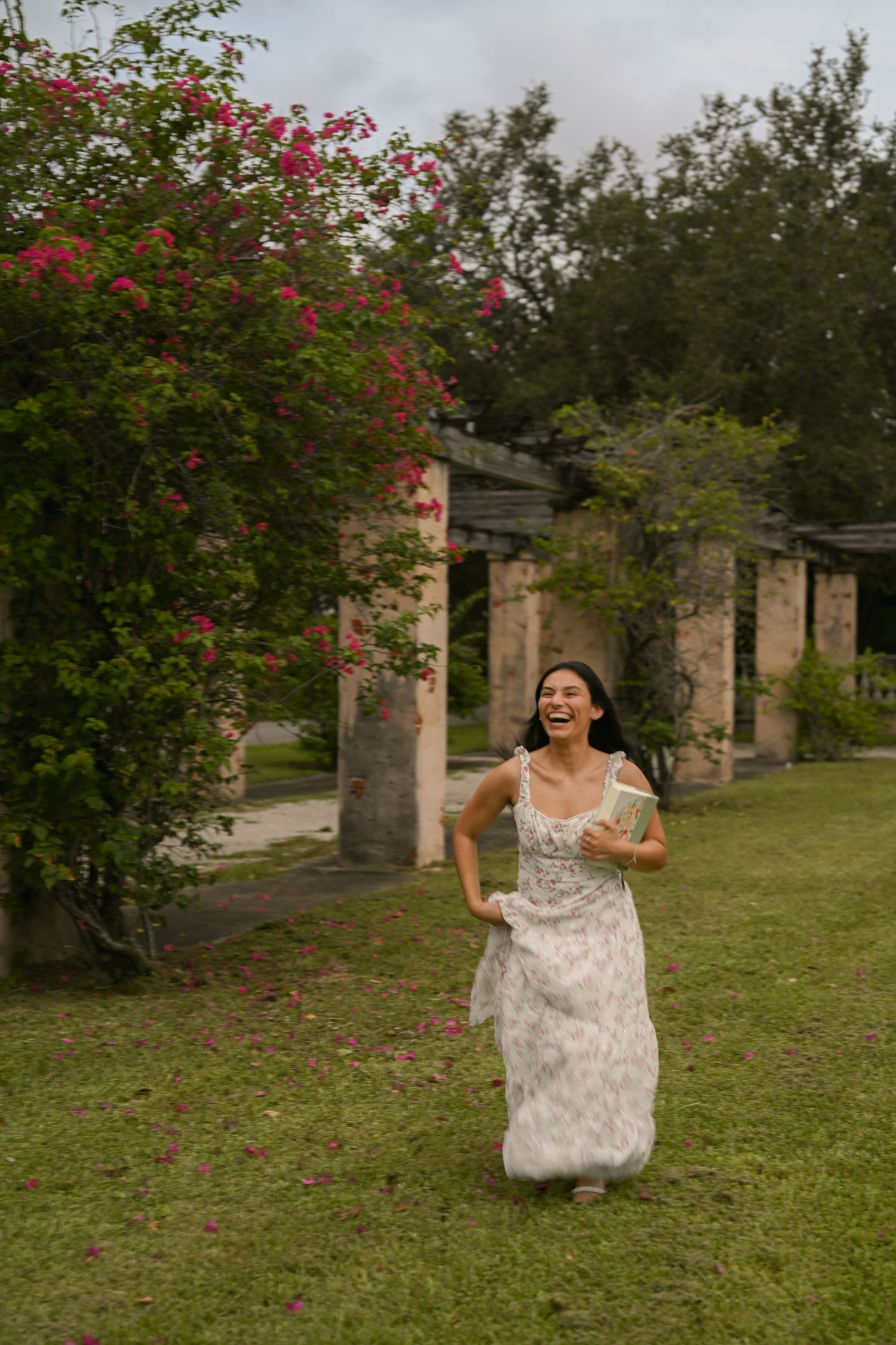 A person in a floral dress runs joyfully through a garden with stone columns.