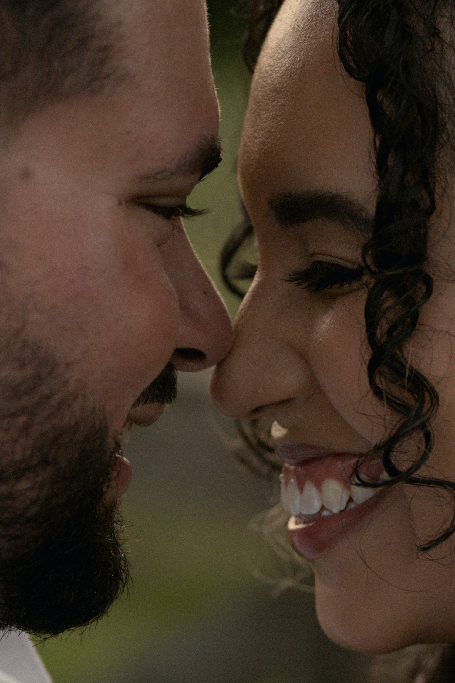 Close-up of a smiling interracial couple sharing an intimate moment, faces nearly touching, man with beard and woman with curly hair.