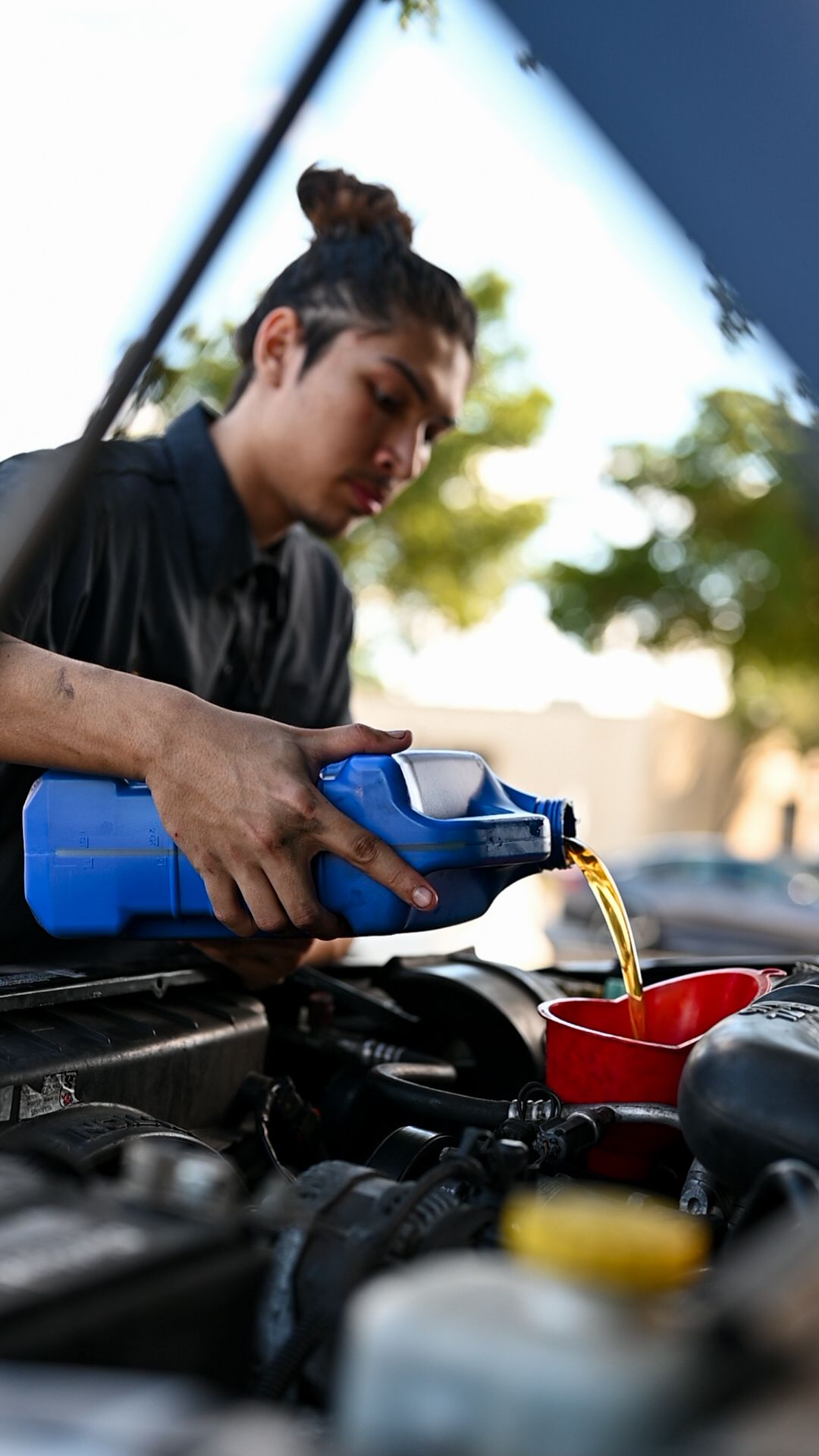 Person pouring motor oil into a car engine during routine vehicle maintenance at sunset.