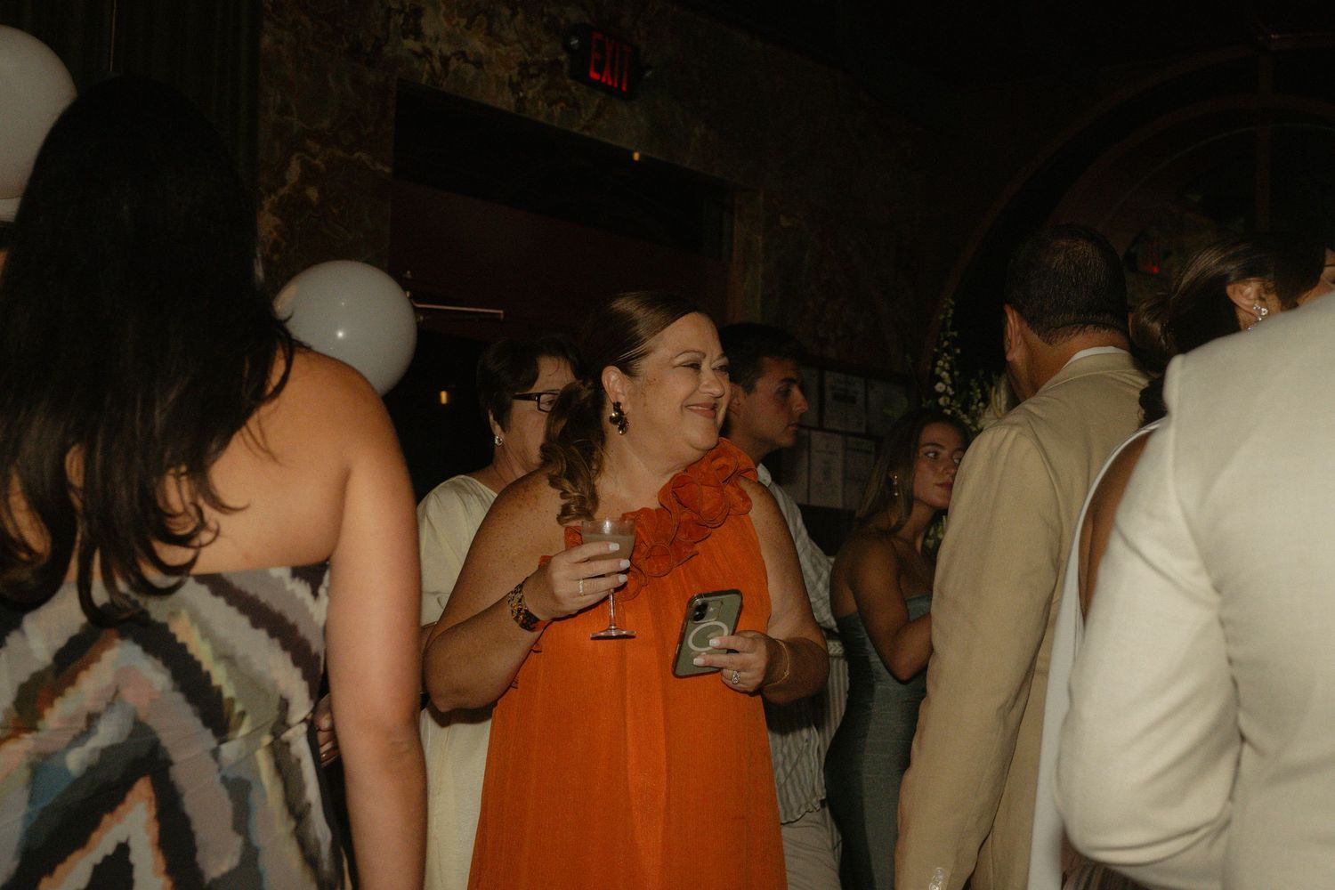 Woman in orange dress holding a drink at an elegant indoor party event.