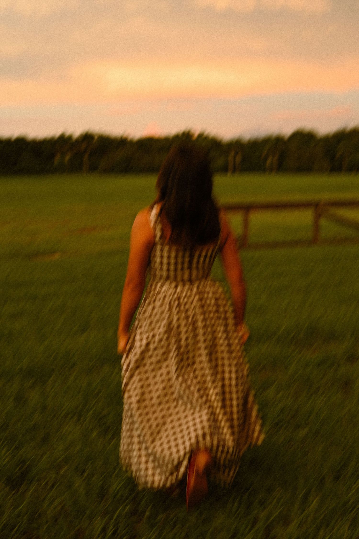 Figure in black and white dress moves through tall grass during sunset.