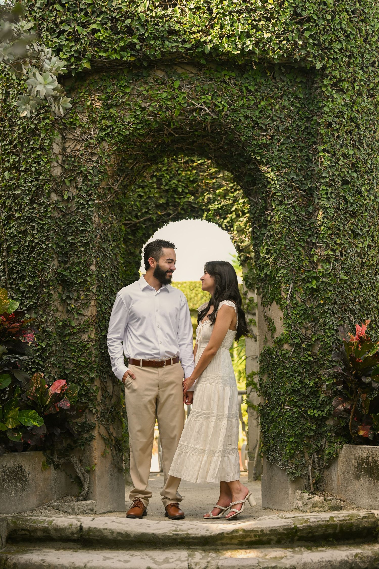 A romantic couple shares intimate moments against an ivy-covered wall in a garden setting.