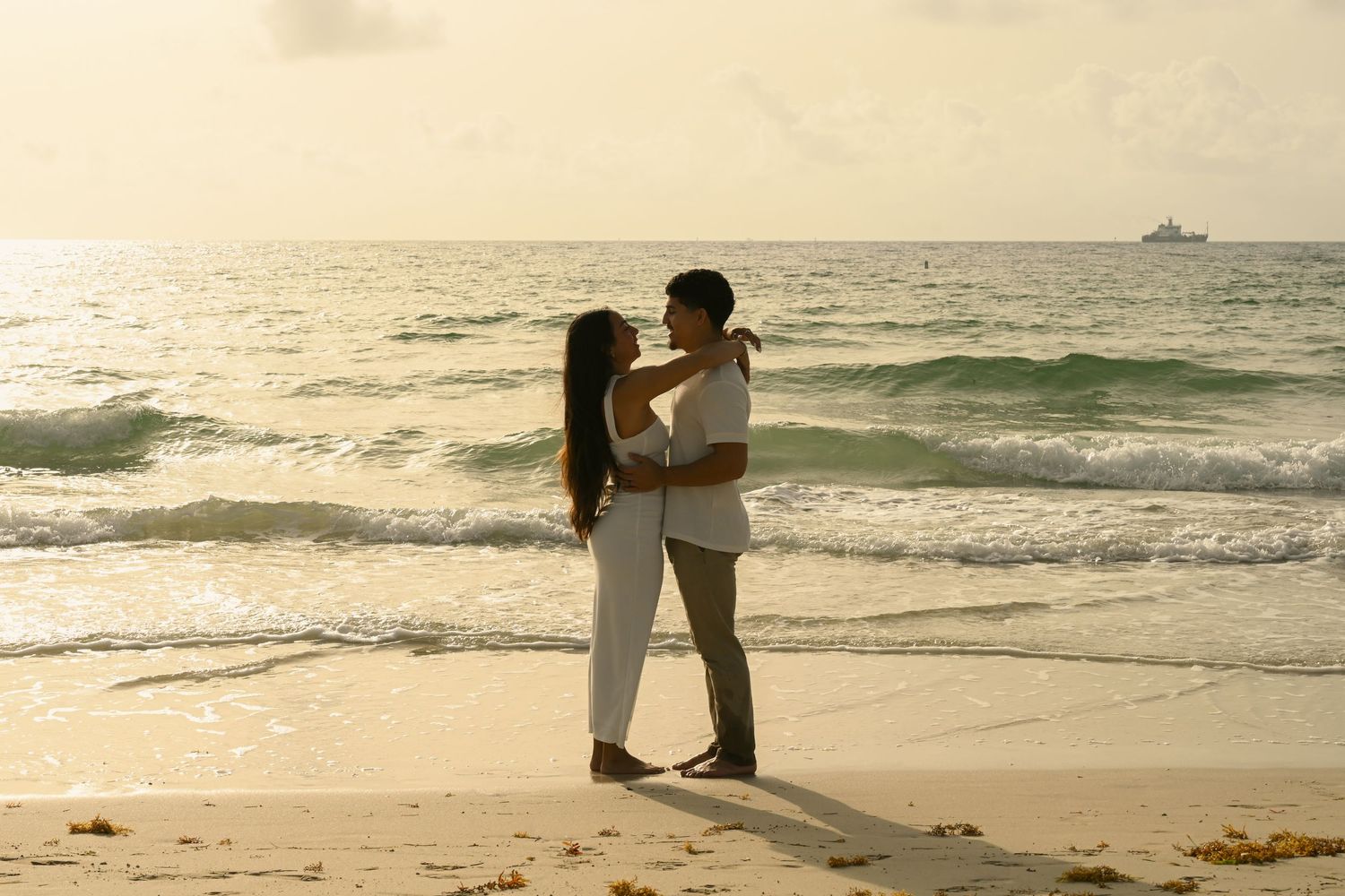 Couple in light colored clothing sharing an intimate moment on the beach at dusk.