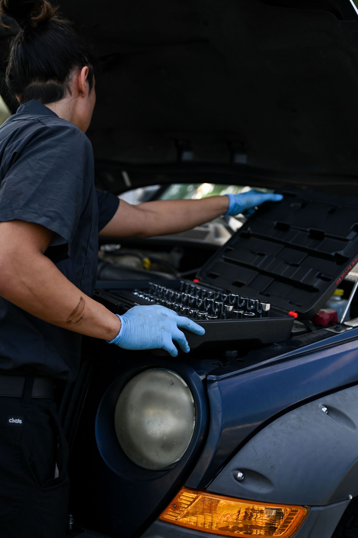 Mechanic performing maintenance work under the hood of a dark colored vehicle.