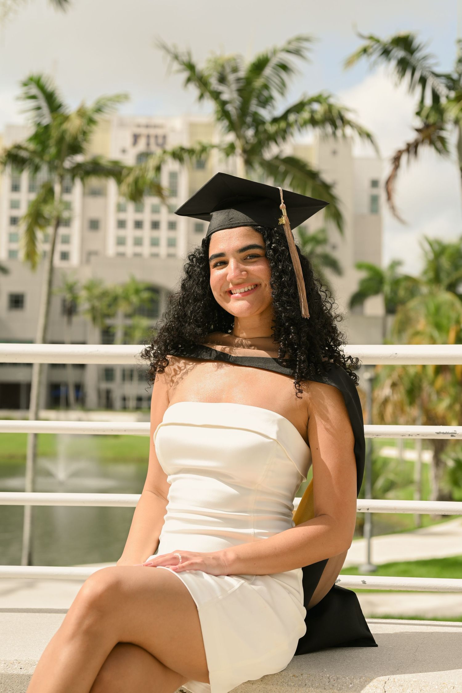 Graduate in cap and gown relaxes on campus grounds during photo session.