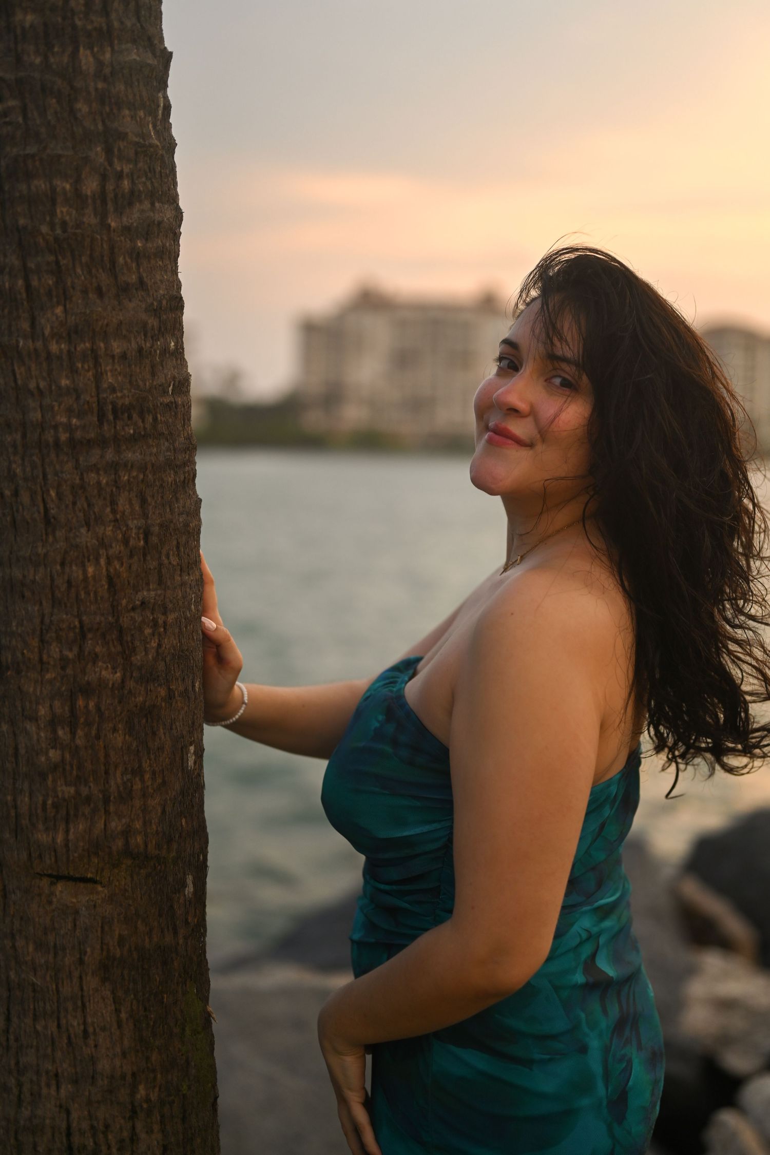 Dramatic portrait series in teal dress with palm tree and coastal backdrop.