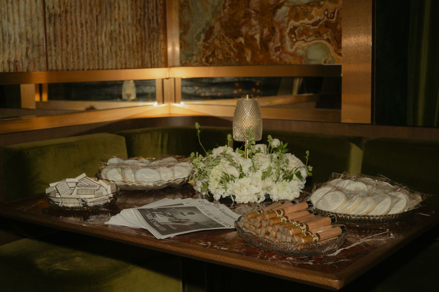 Elegant table display with white floral centerpiece, decorative dishes, and a candle in a cozy green-upholstered booth setting.