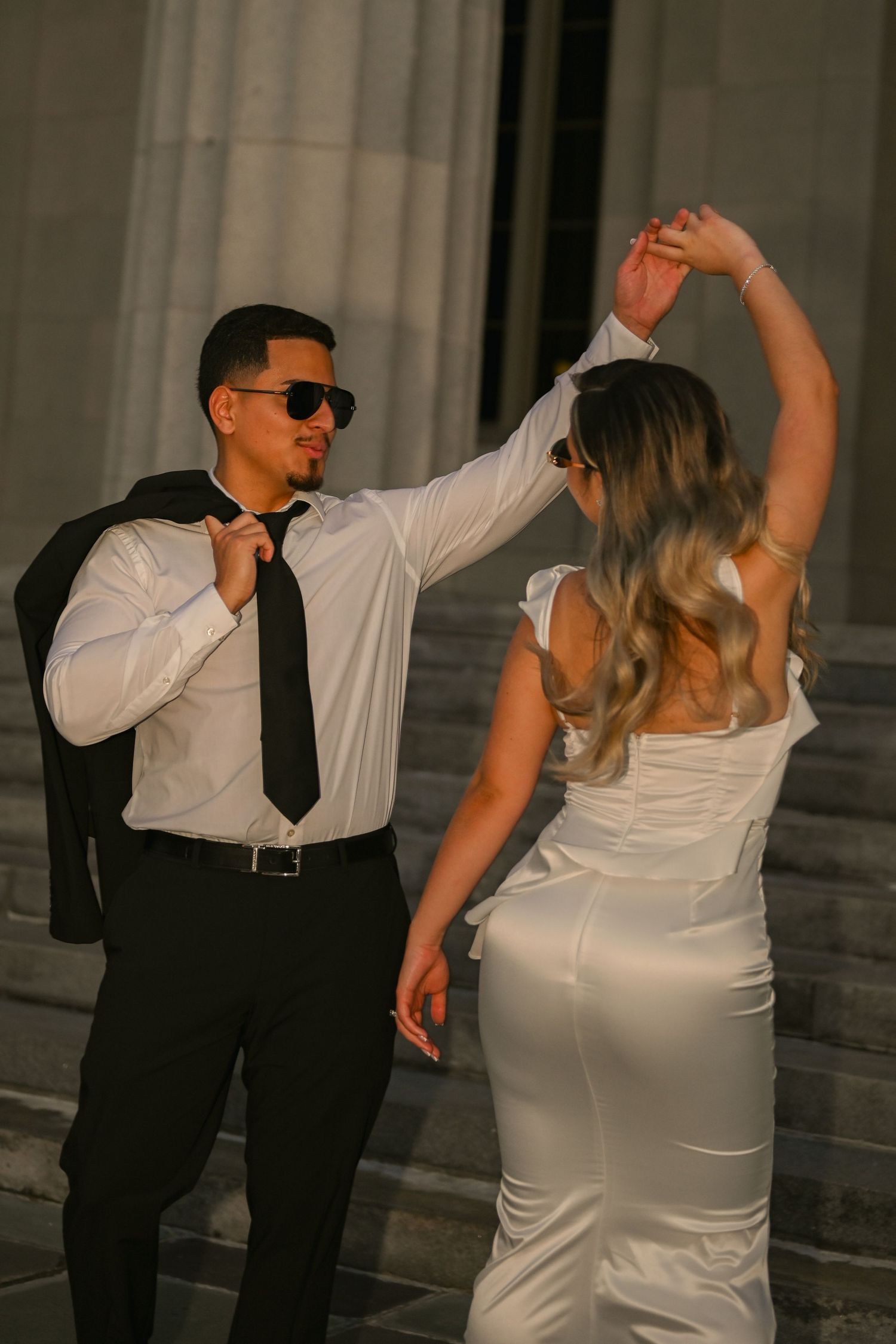 Newlyweds dancing together on steps of a historic building with columns.