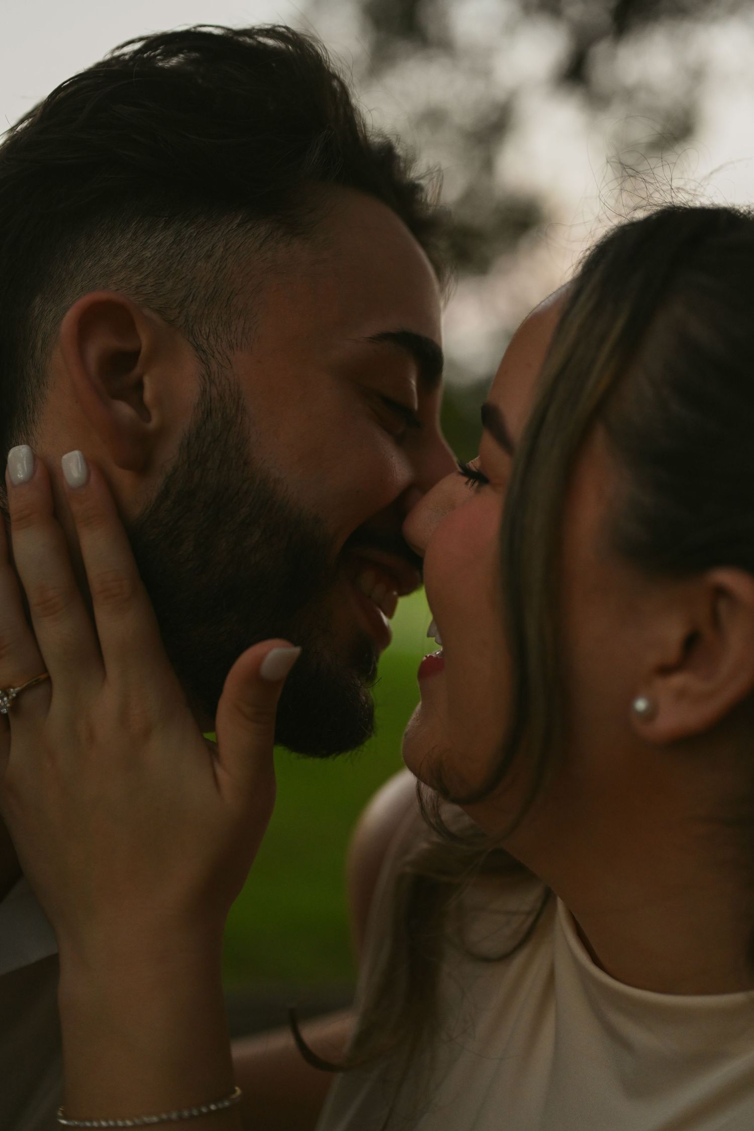 A close-up tender moment between a couple sharing a gentle kiss outdoors.