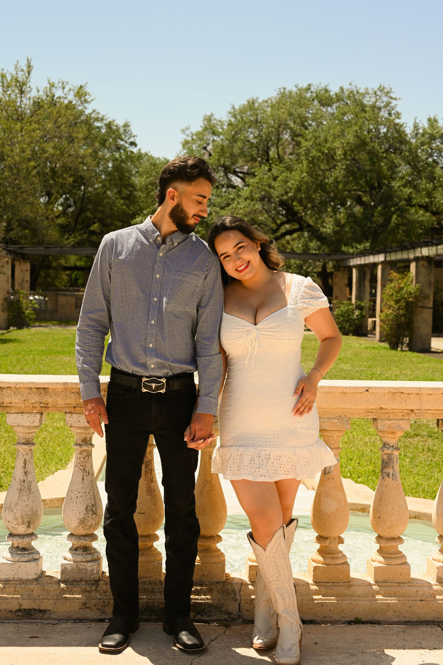 A couple poses together on stone balustrade in a classical garden setting.