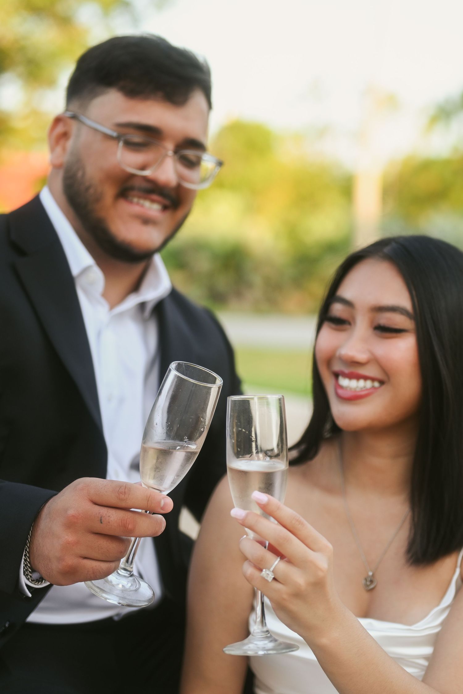 A couple shares champagne glasses during an outdoor celebration with natural lighting.