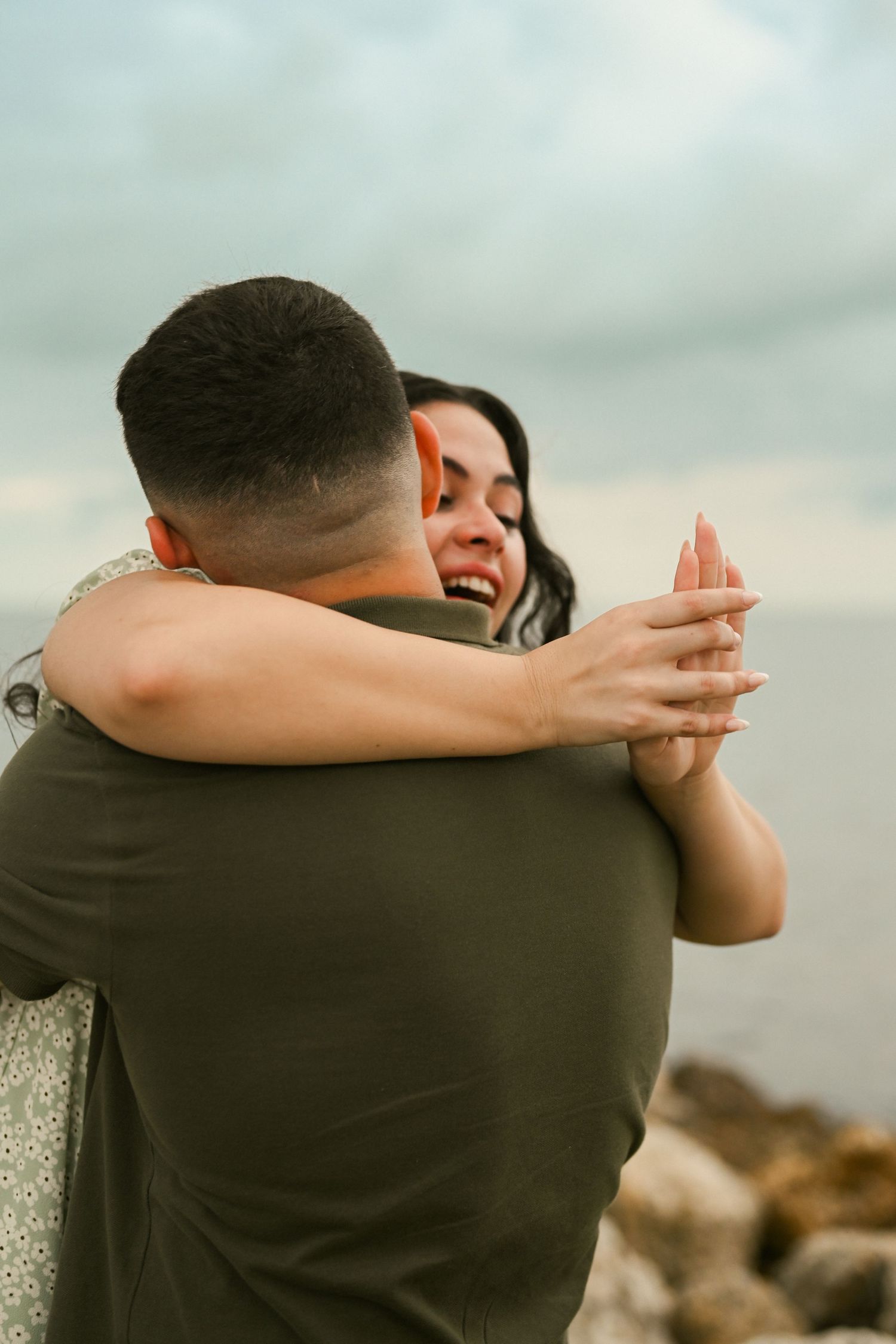 A romantic couple embraces while standing against a cloudy sky backdrop.
