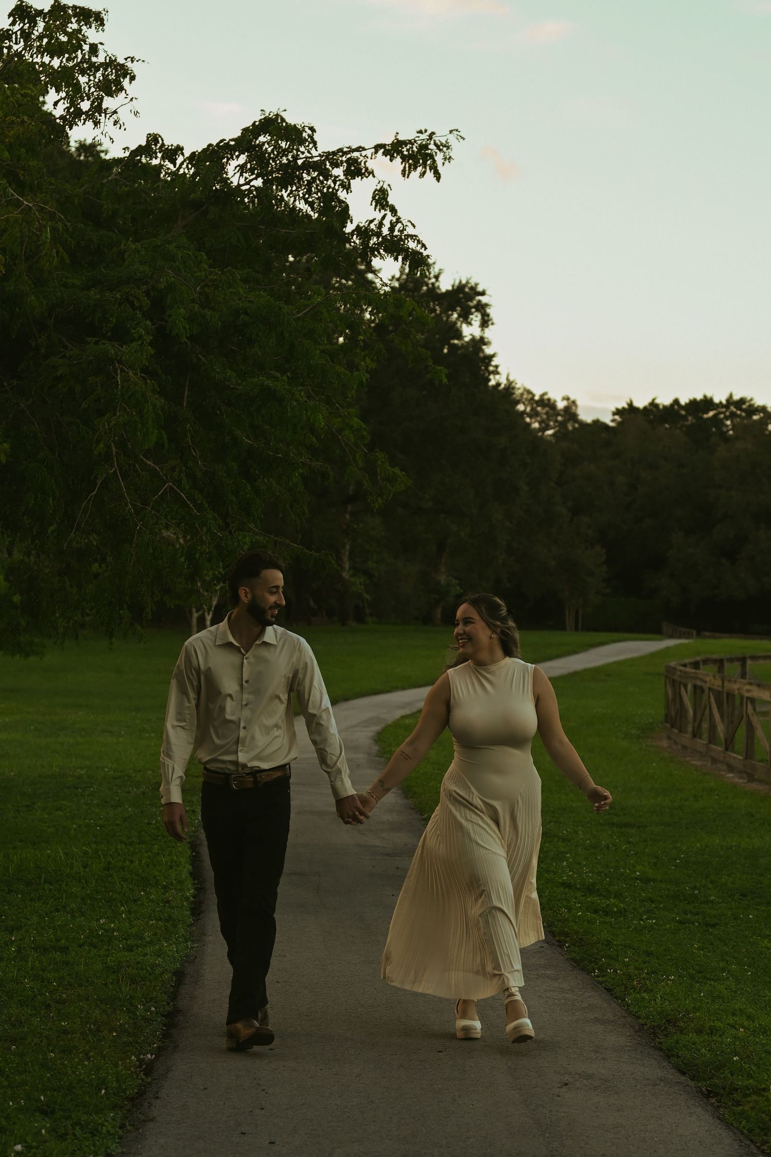 A couple strolling hand in hand along a park pathway at dusk.