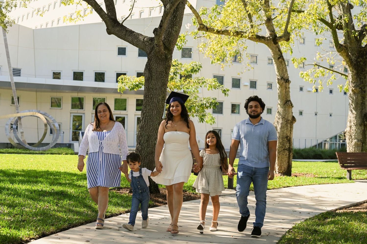 Group walking along a campus sidewalk with white buildings and trees in background.