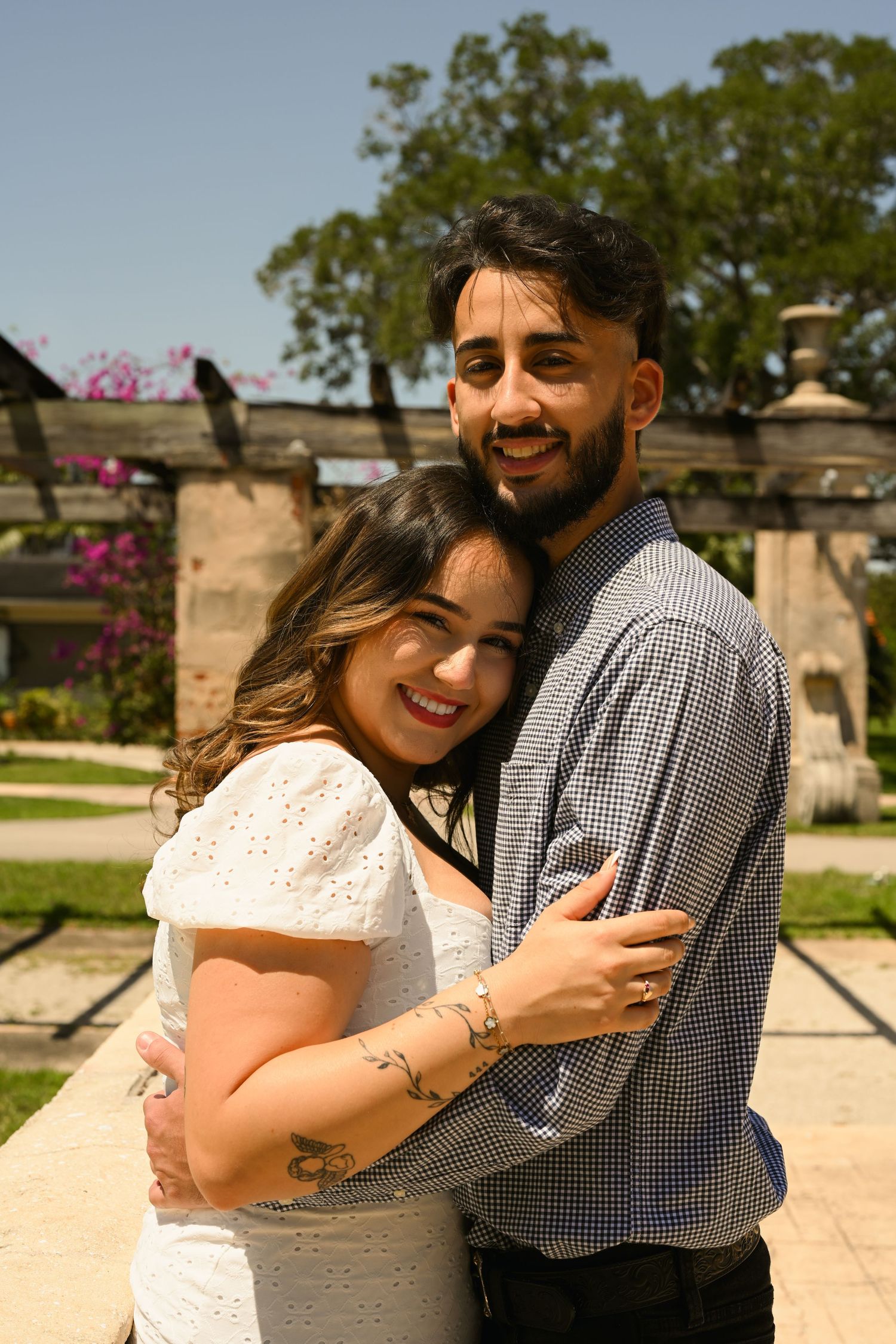A joyful embrace captured in a sunlit garden with blooming flowers and stone architecture.