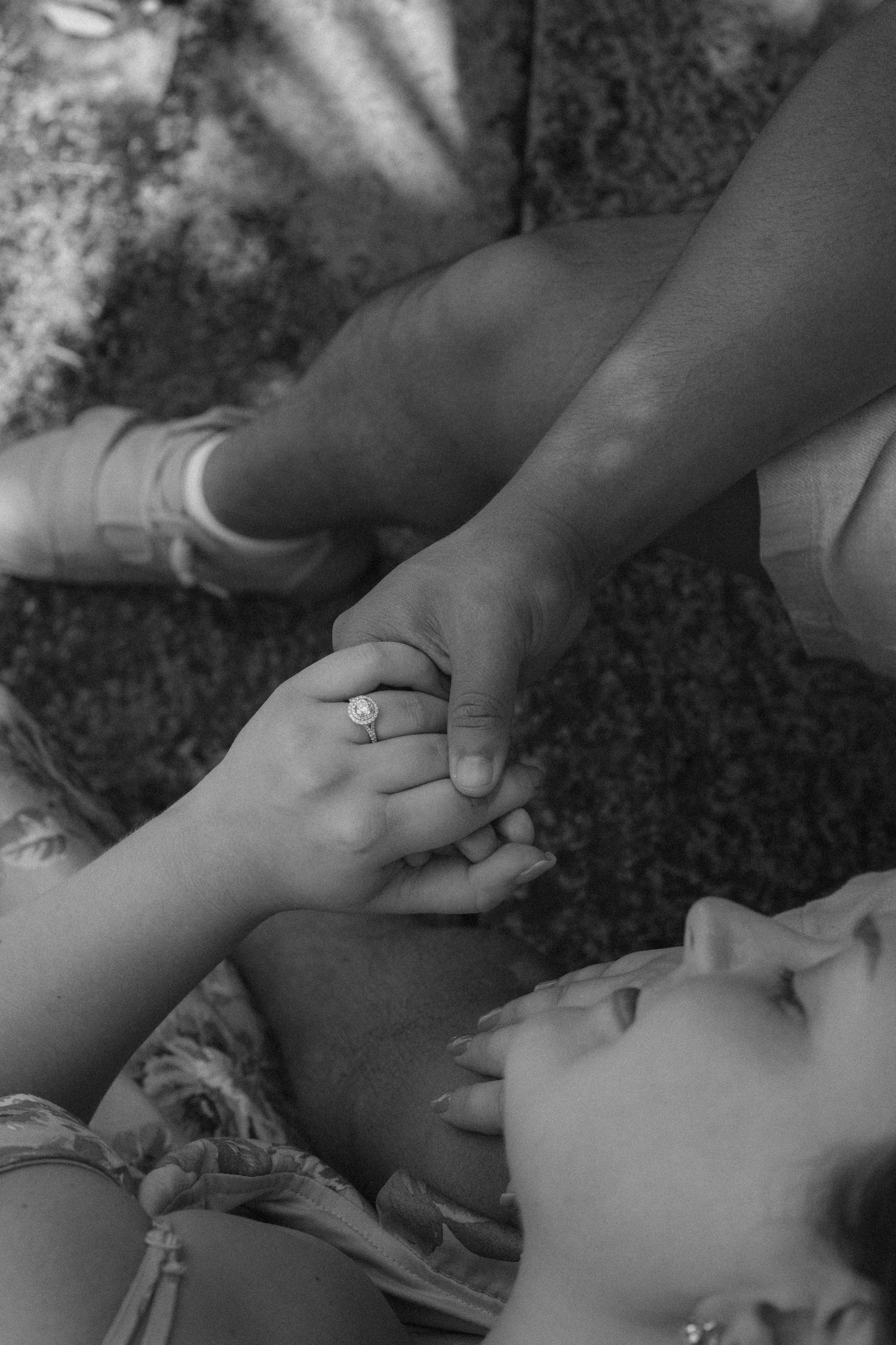 Black and white photo of a couple holding hands, woman wearing engagement ring, romantic outdoor proposal moment.