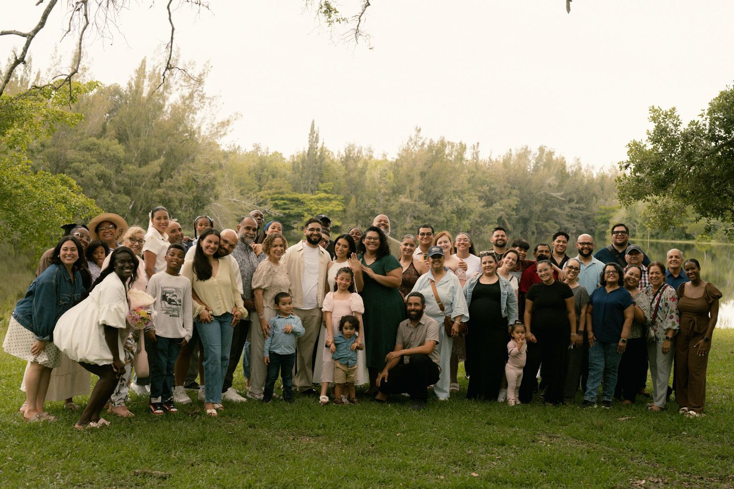 Large group of family and friends pose together for a photo in a lush green outdoor setting.