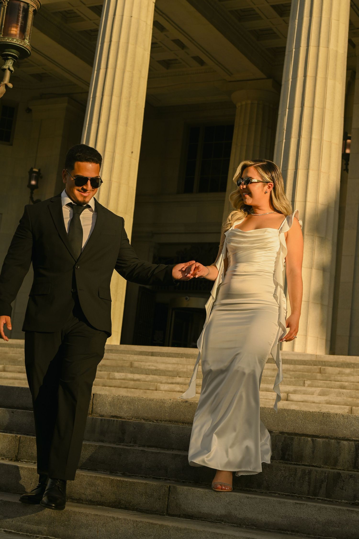 A bride and groom share a romantic moment between classic stone columns at sunset.