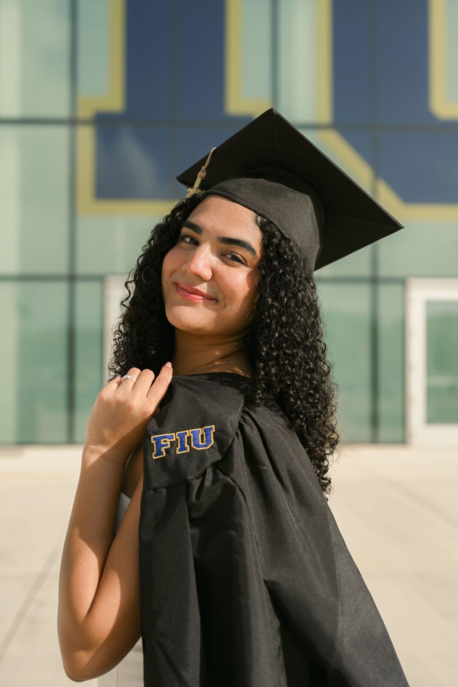 Graduate in black cap and gown smiling during graduation photo session at FIU campus.