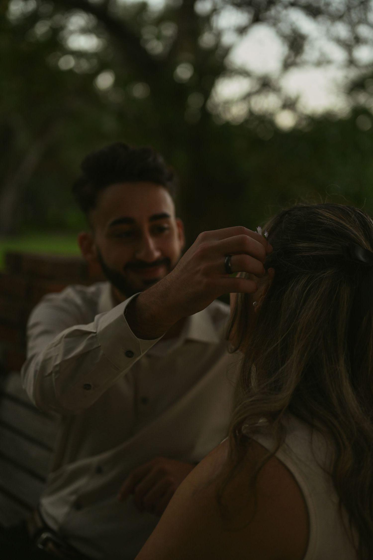 An intimate moment captured between a couple sitting on a wooden bench at dusk.