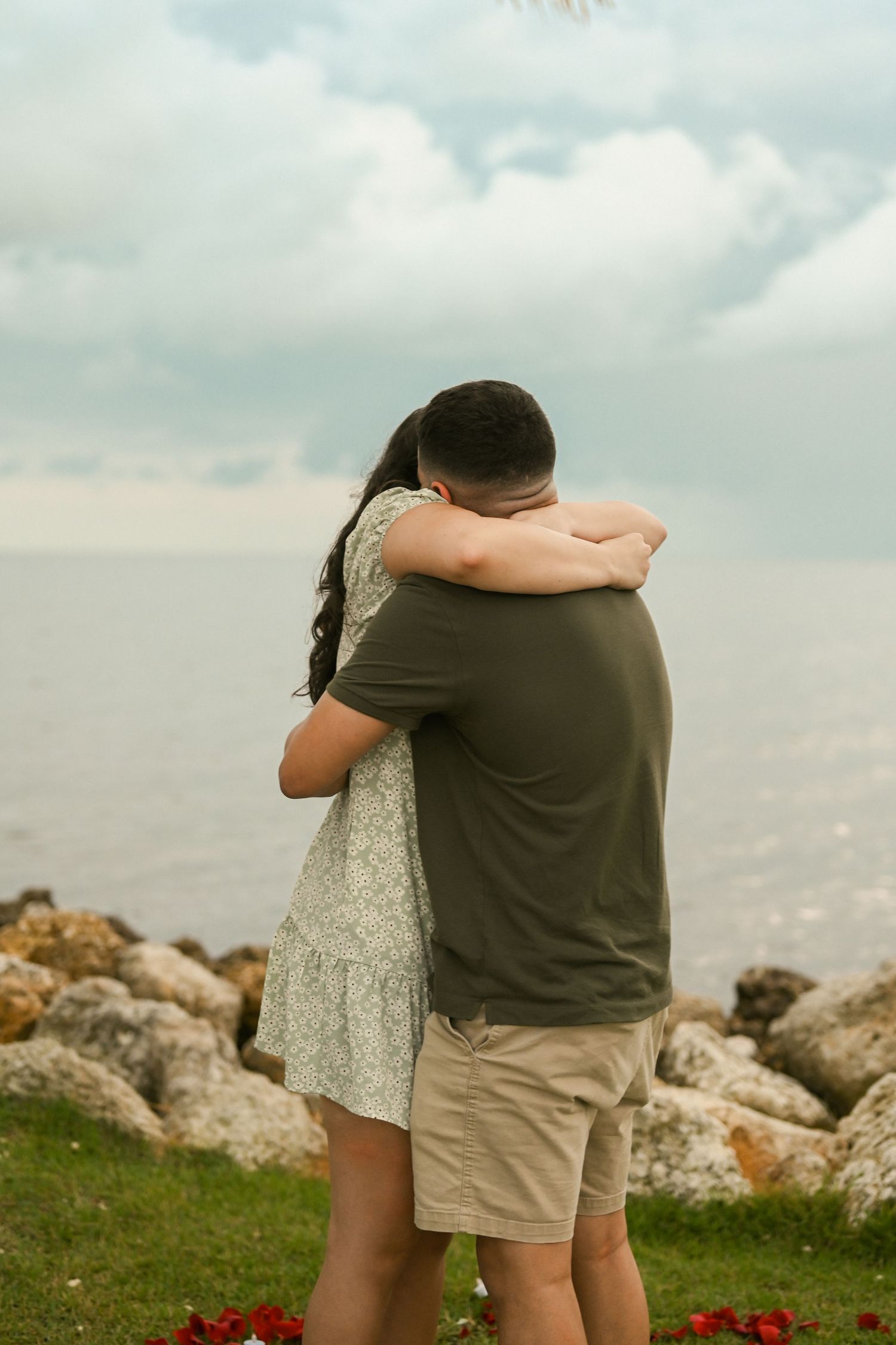 A couple shares an intimate embrace by the ocean after getting engaged.