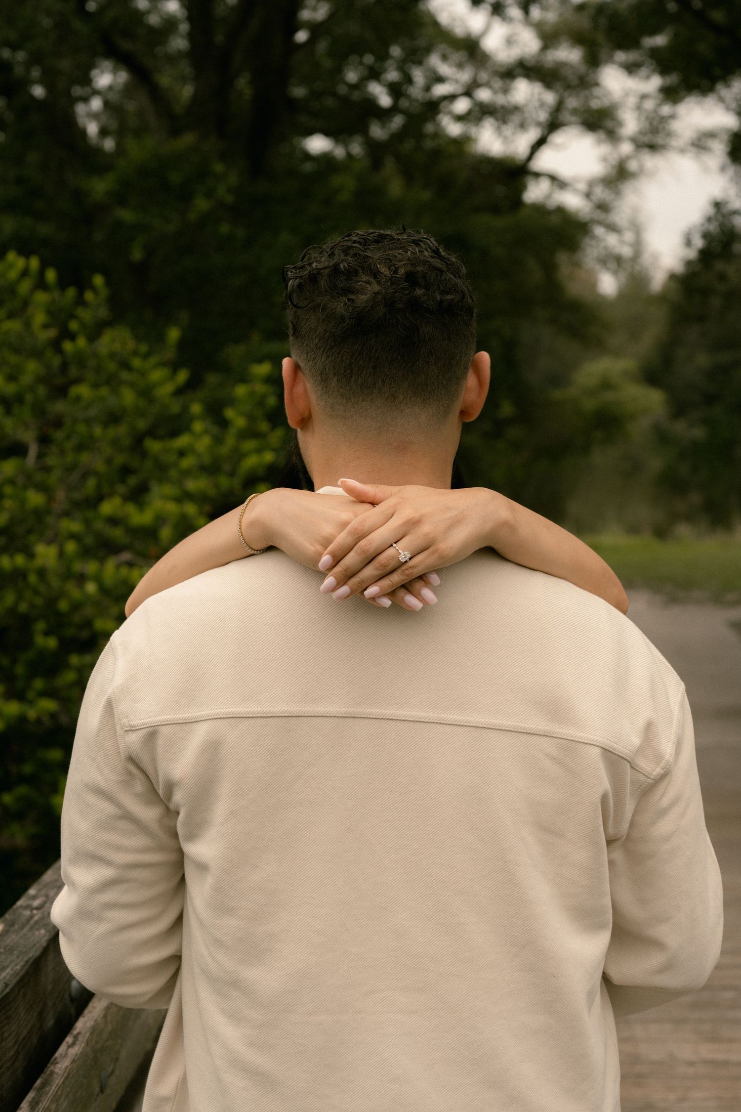 Close-up of woman's hand with ring resting on man's shoulder in beige jacket.