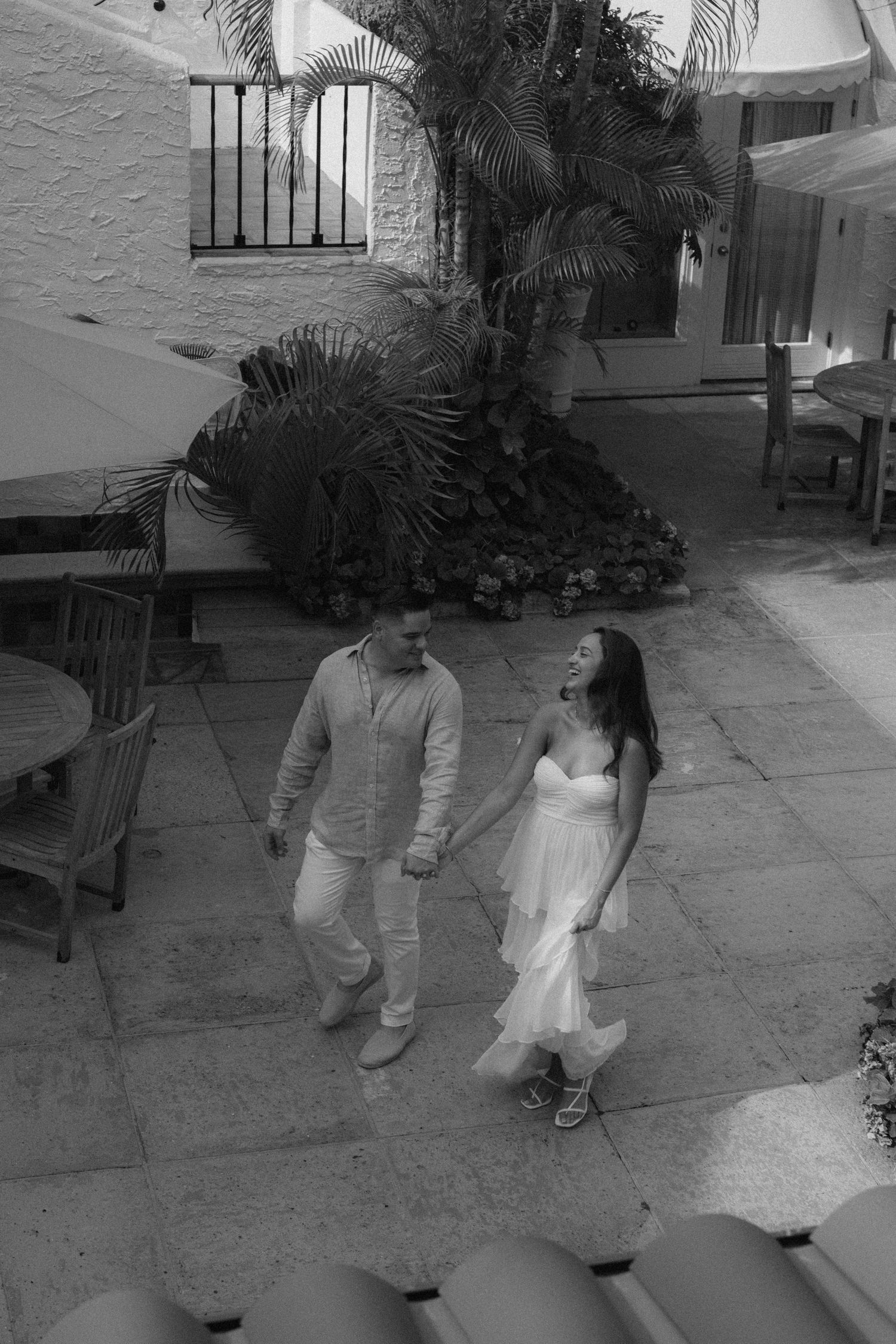 Black and white photo of a couple holding hands walking through a courtyard.
