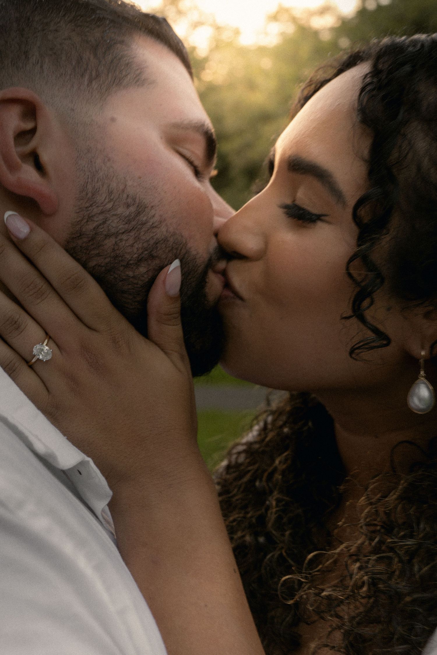 Close-up of an engaged couple sharing a romantic kiss, showcasing a sparkling diamond engagement ring.