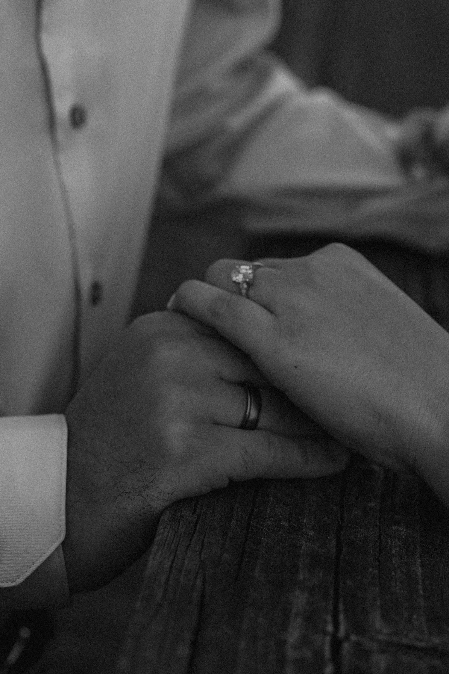 Close-up of hands with engagement rings resting on a wooden surface.