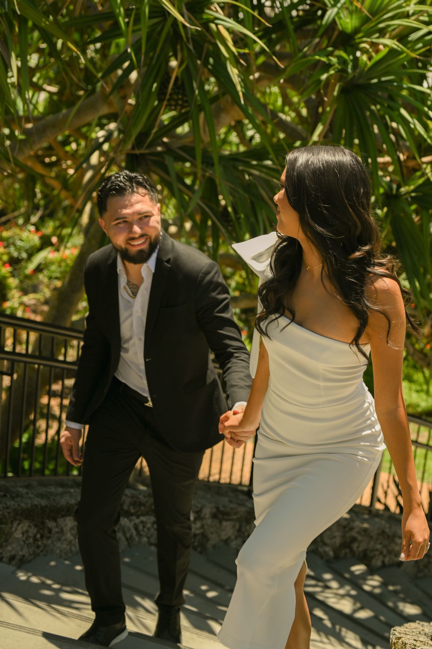 A couple shares candid moments on stone steps surrounded by tropical plants.