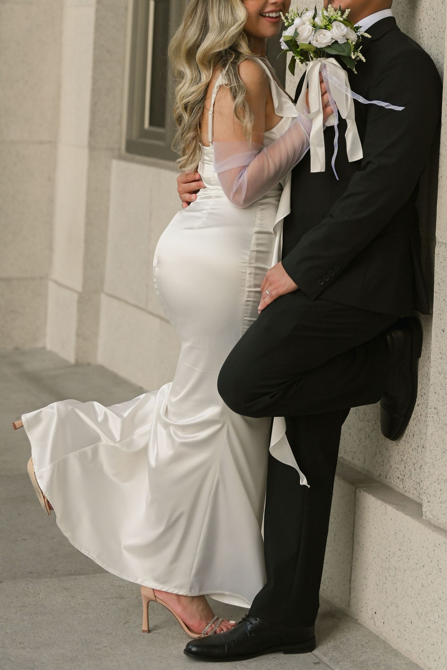 Playful wedding pose with bride's dress flowing against courthouse backdrop.