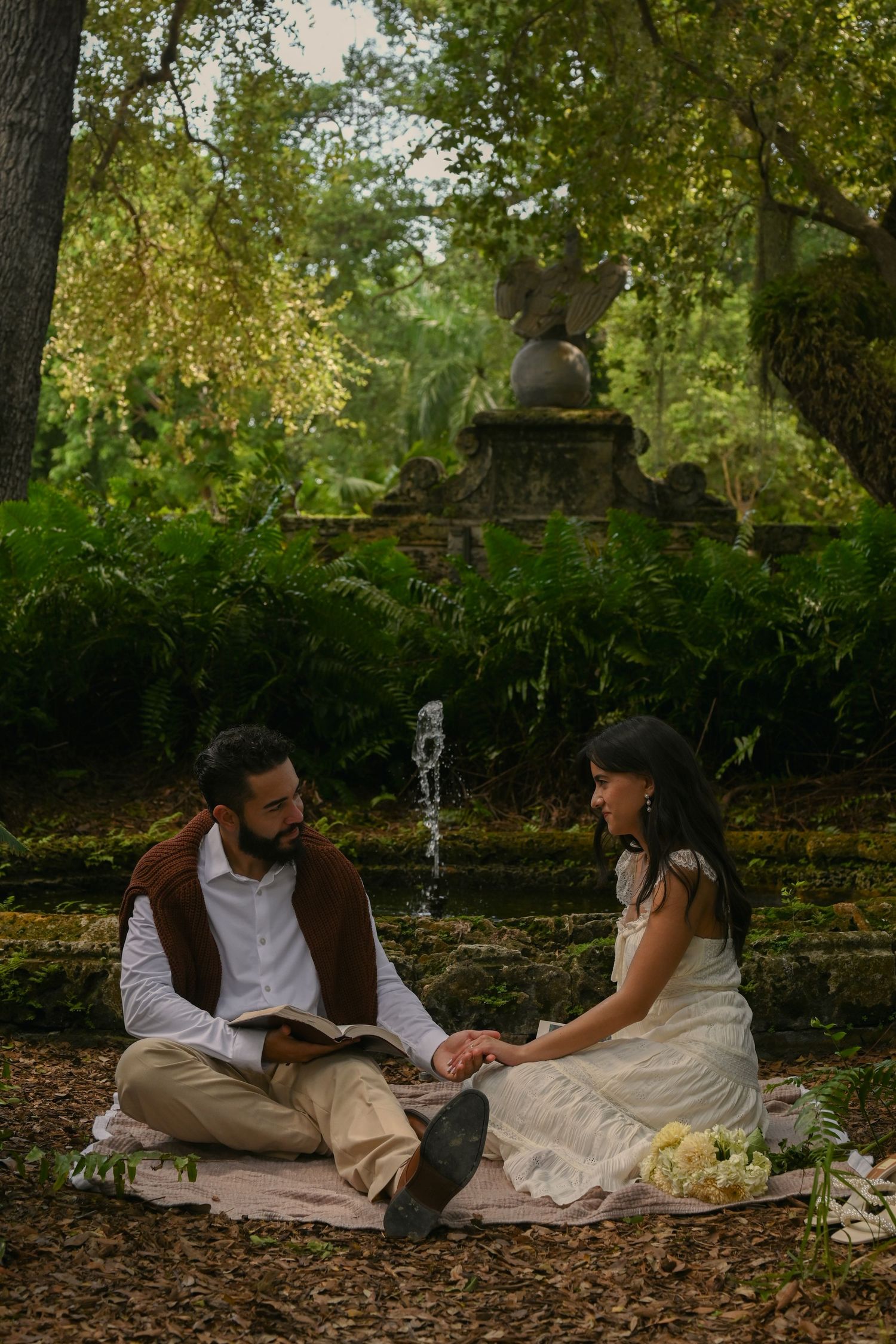 A couple enjoys a romantic picnic together on fallen leaves in an autumn garden setting.