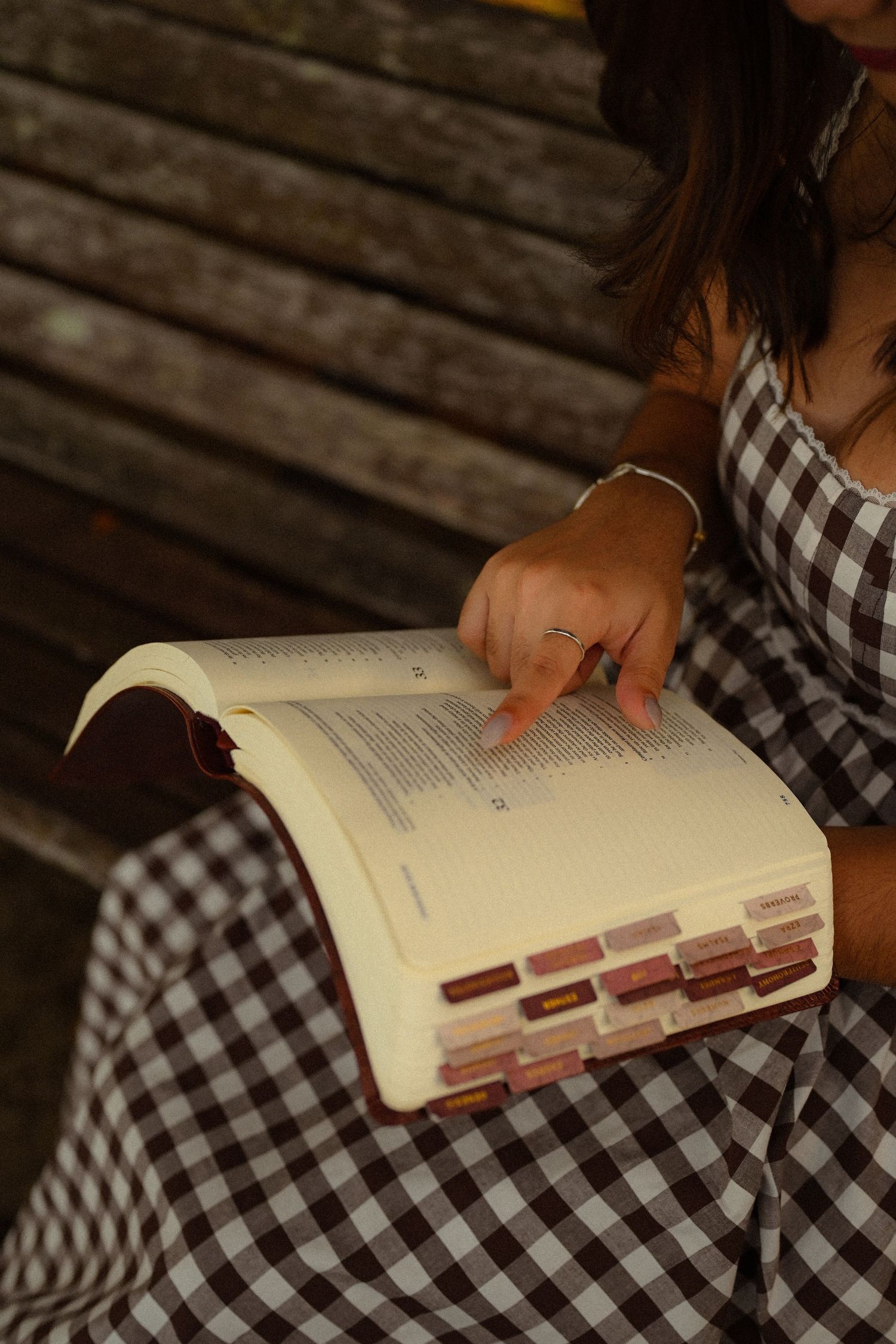 Close-up of hands holding open book while wearing black and white checkered dress.