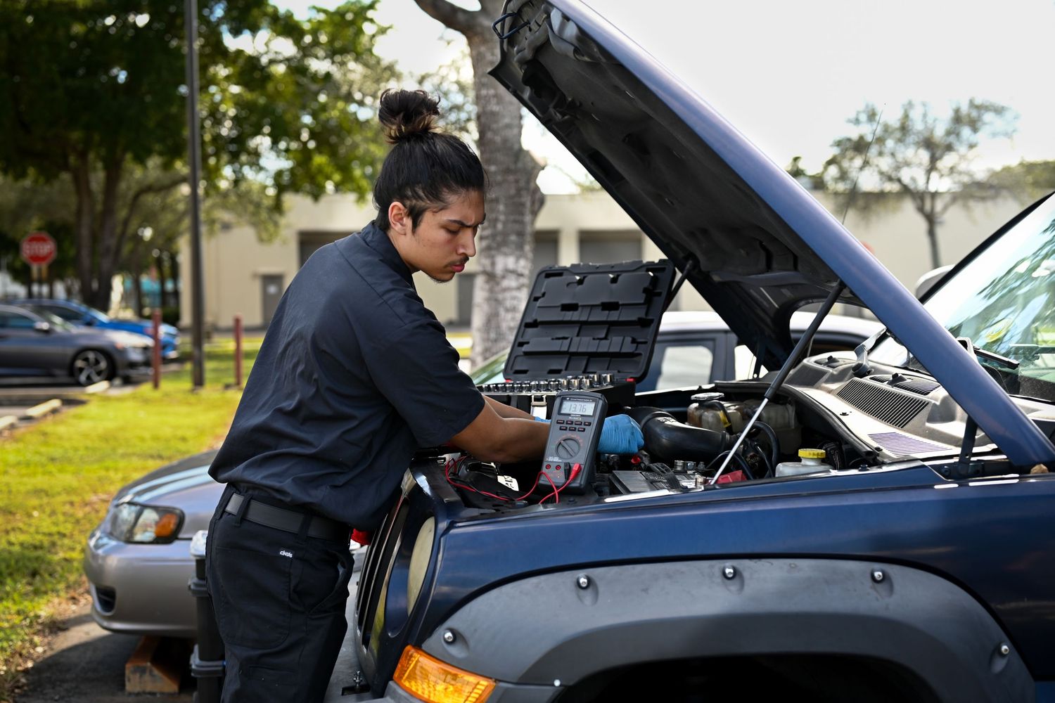 Mechanic performing maintenance checks under an open car hood.