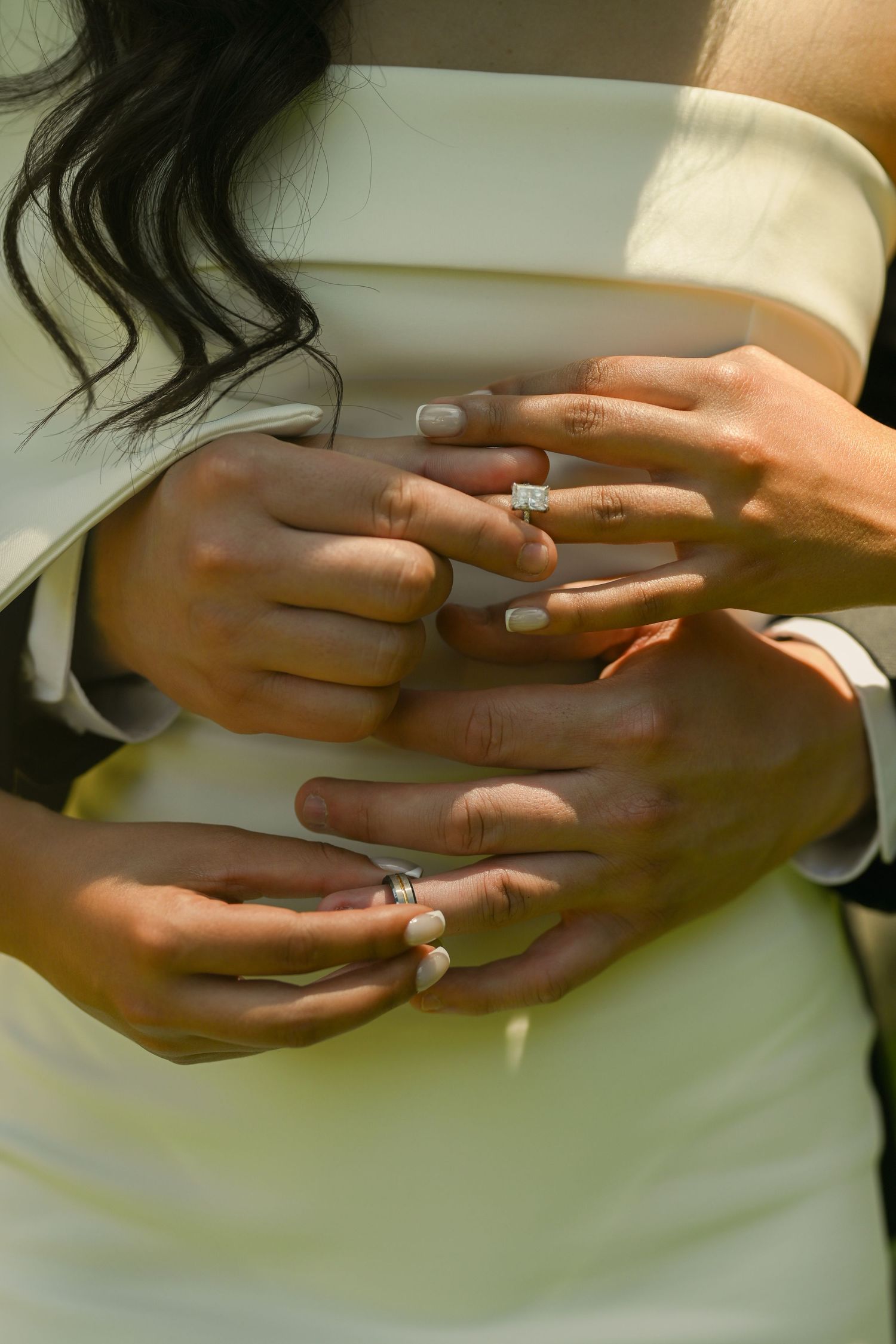 Close-up of hands with wedding rings touching tenderly against a light background.